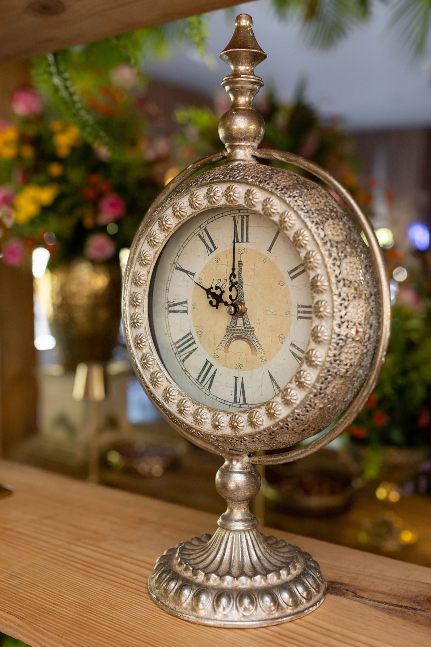 Ornate vintage silver mantel clock with Eiffel Tower dial and Roman numerals surrounded by colorful flowers.