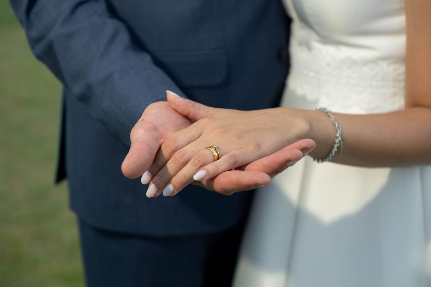 Bride and groom holding hands showing gold wedding ring and diamond bracelet on wedding day.