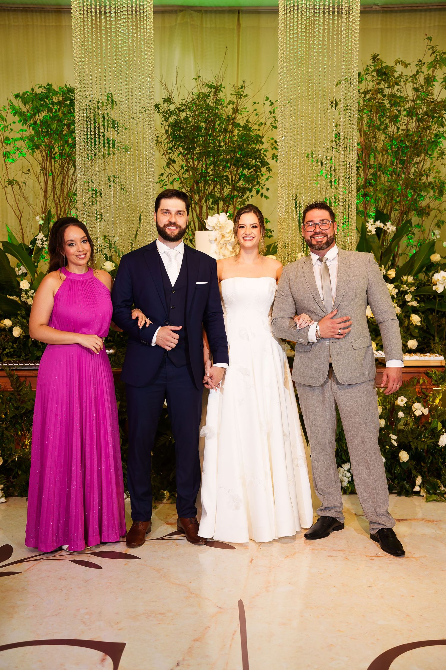 Wedding party poses together, bride in white gown, groom in navy suit, guests in fuchsia dress and gray suit.