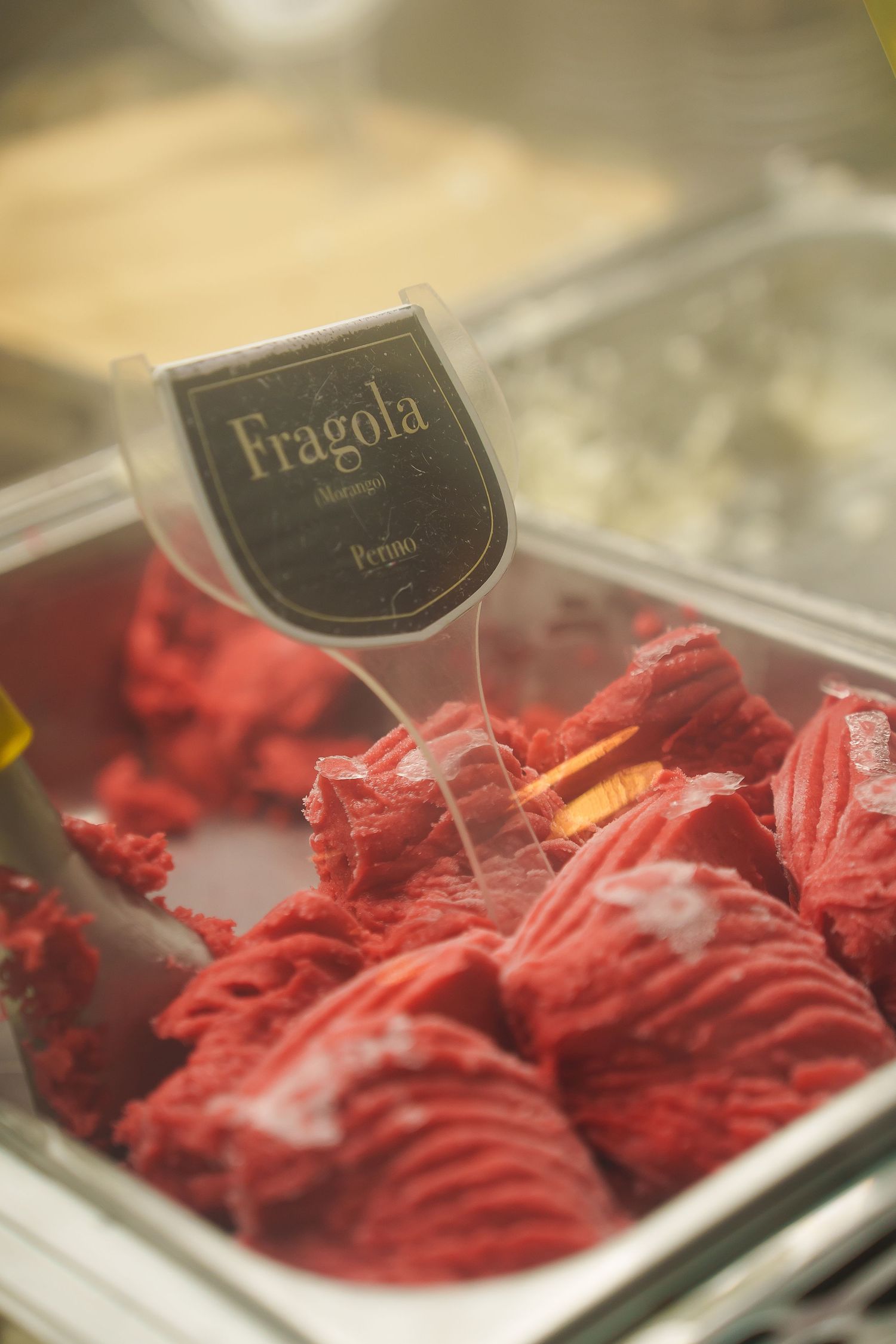 Close-up of vibrant red Fragola strawberry gelato in a display case at an Italian gelateria.