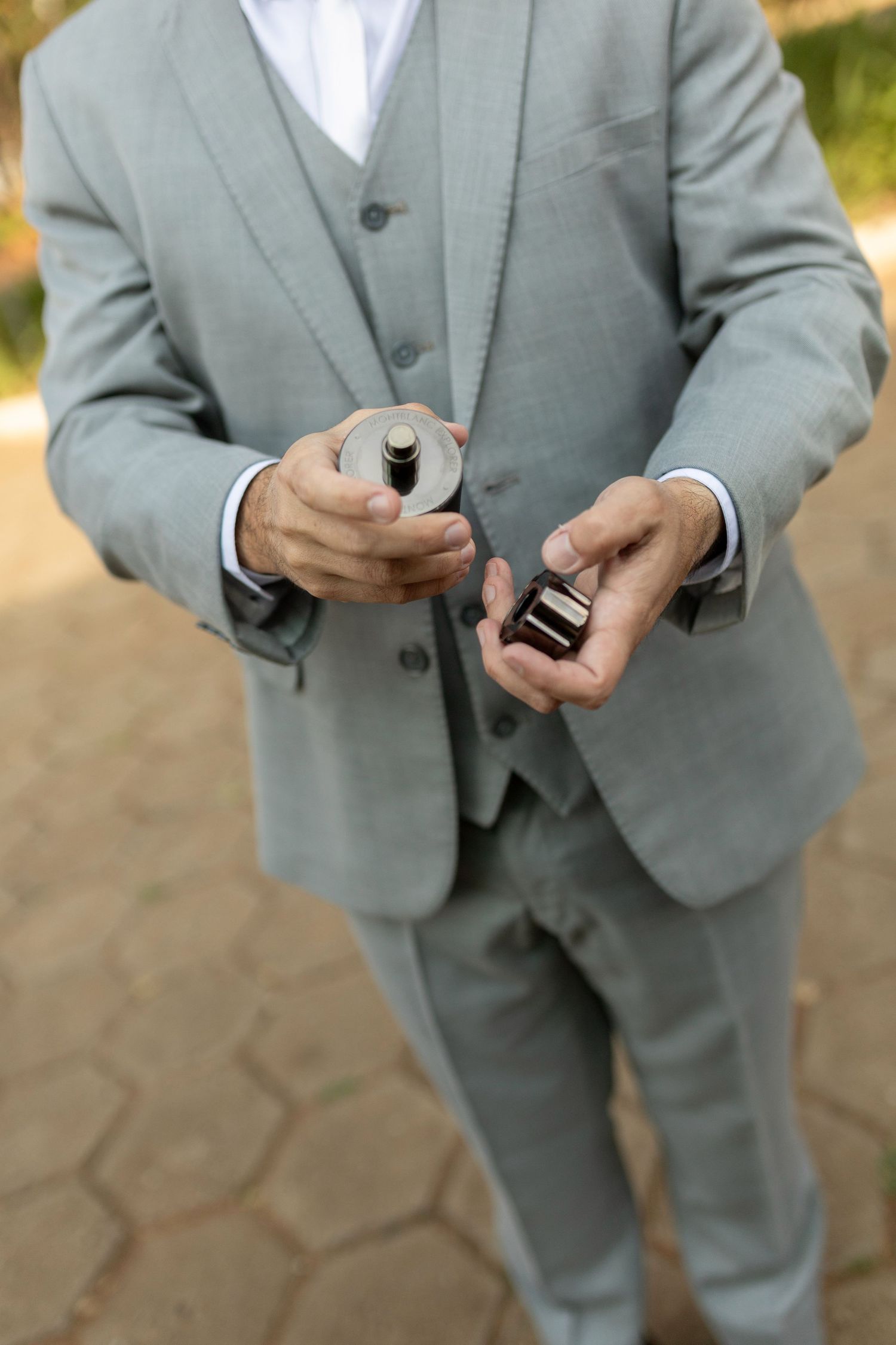 Man in gray suit holding a perfume bottle and open ring box outdoors.