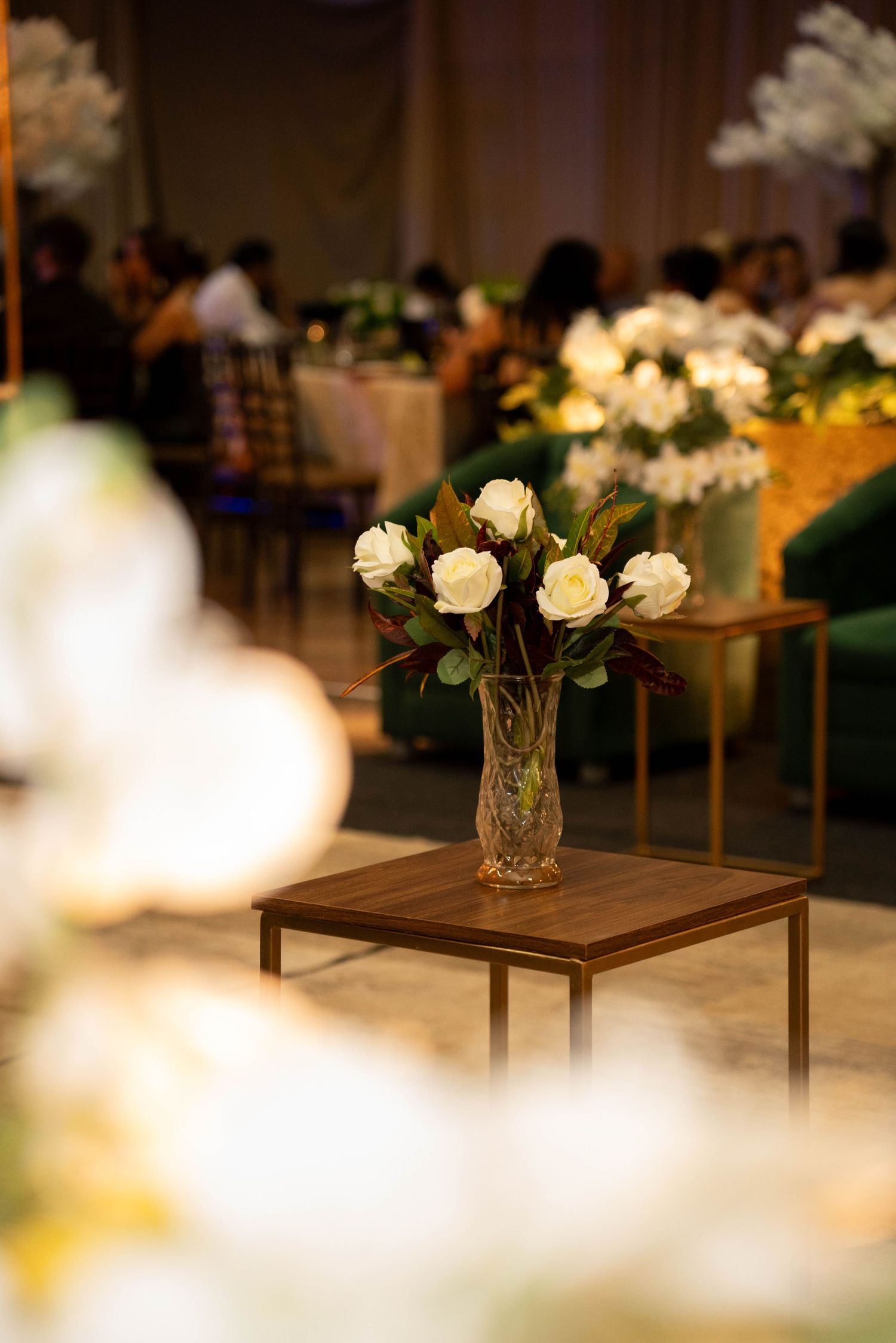 Crystal vase with white roses on wooden table at elegant event venue with soft bokeh lighting.