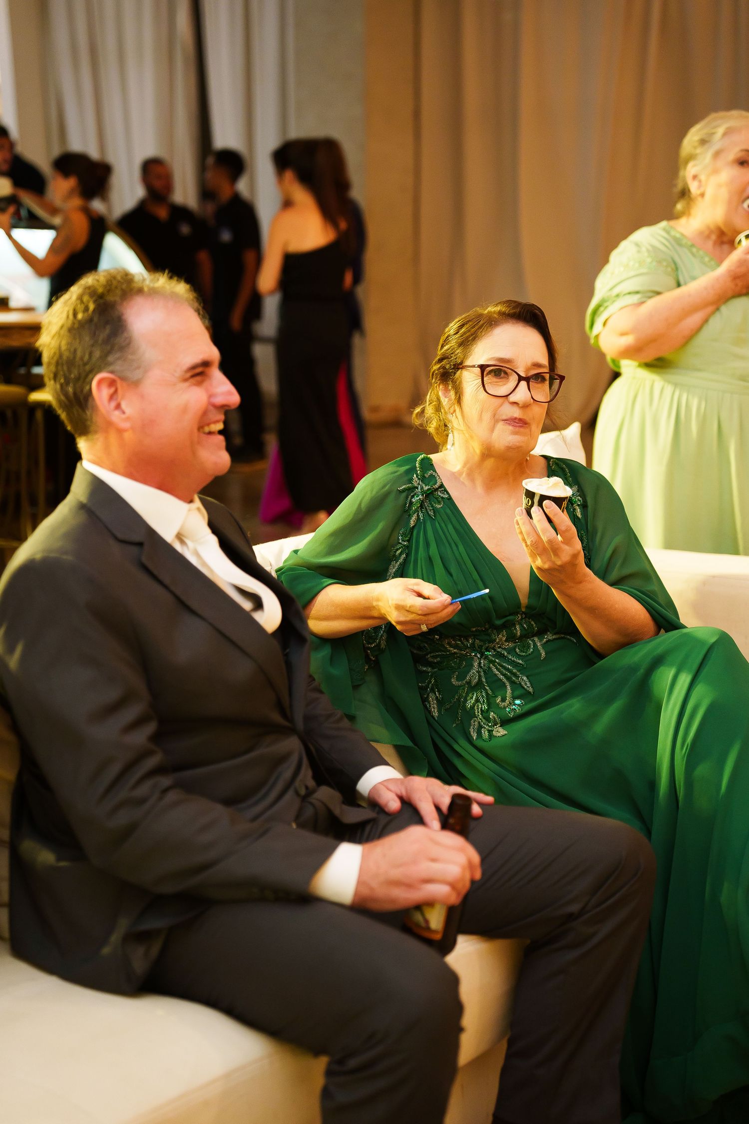 A man in a suit and woman in an elegant green gown sit together at a formal event, smiling and conversing.