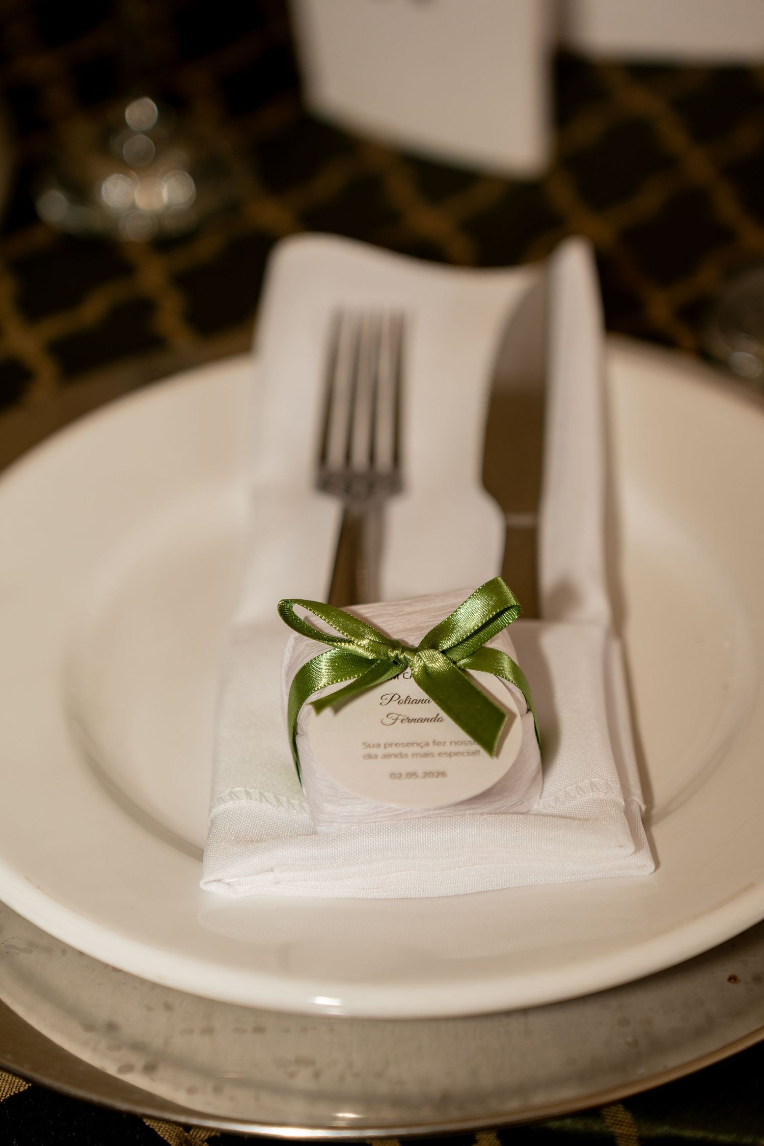 Elegant wedding place setting with white plate, fork, napkin, and green ribbon gift favor on silver charger.