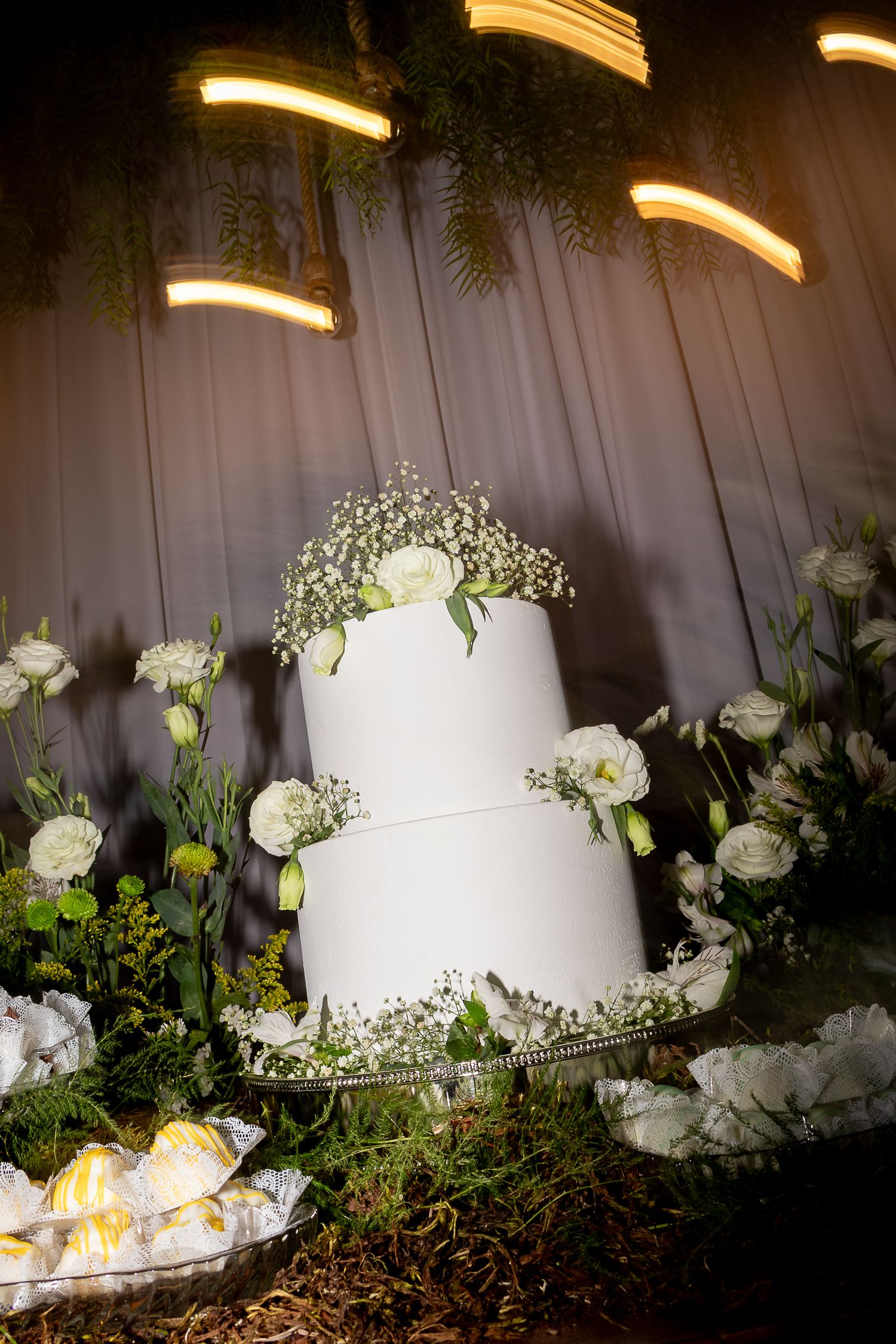 Elegant two-tier white wedding cake adorned with white flowers and greenery on a decorated table.