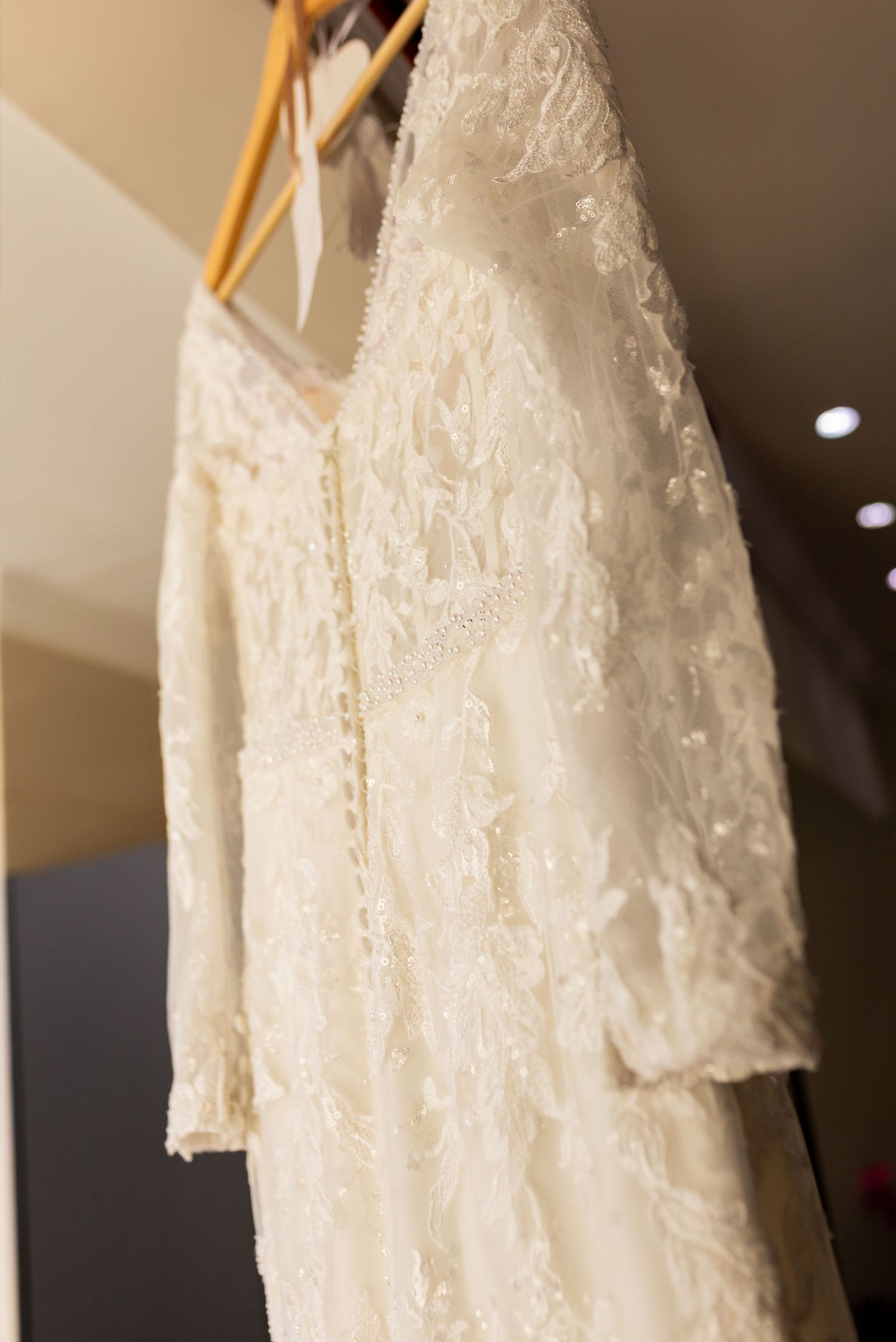 Elegant white lace wedding dress with long sleeves hanging on wooden hangers in a bridal boutique.