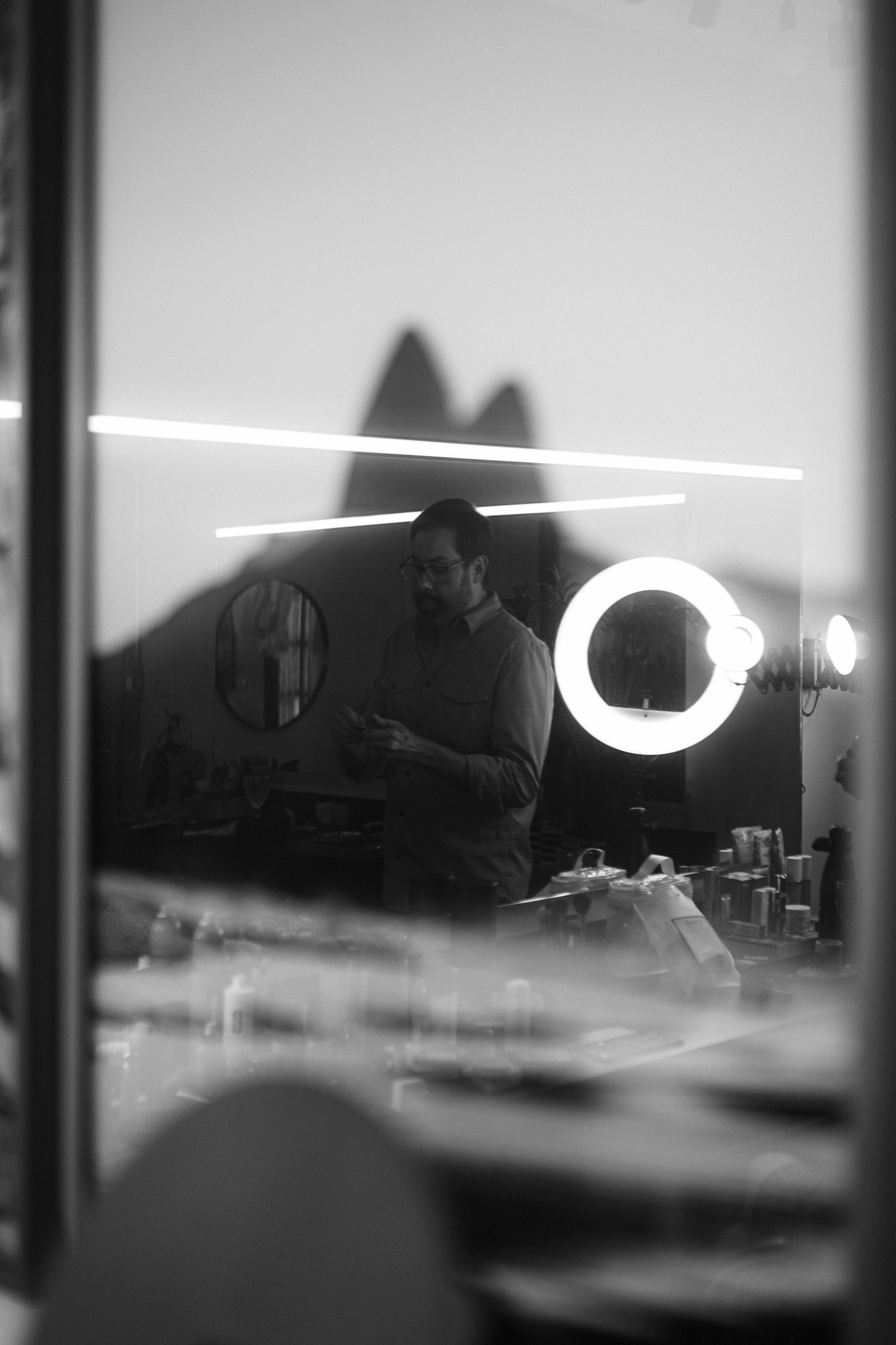 Black and white mirror selfie of a bearded man in a barbershop with ring light reflection.