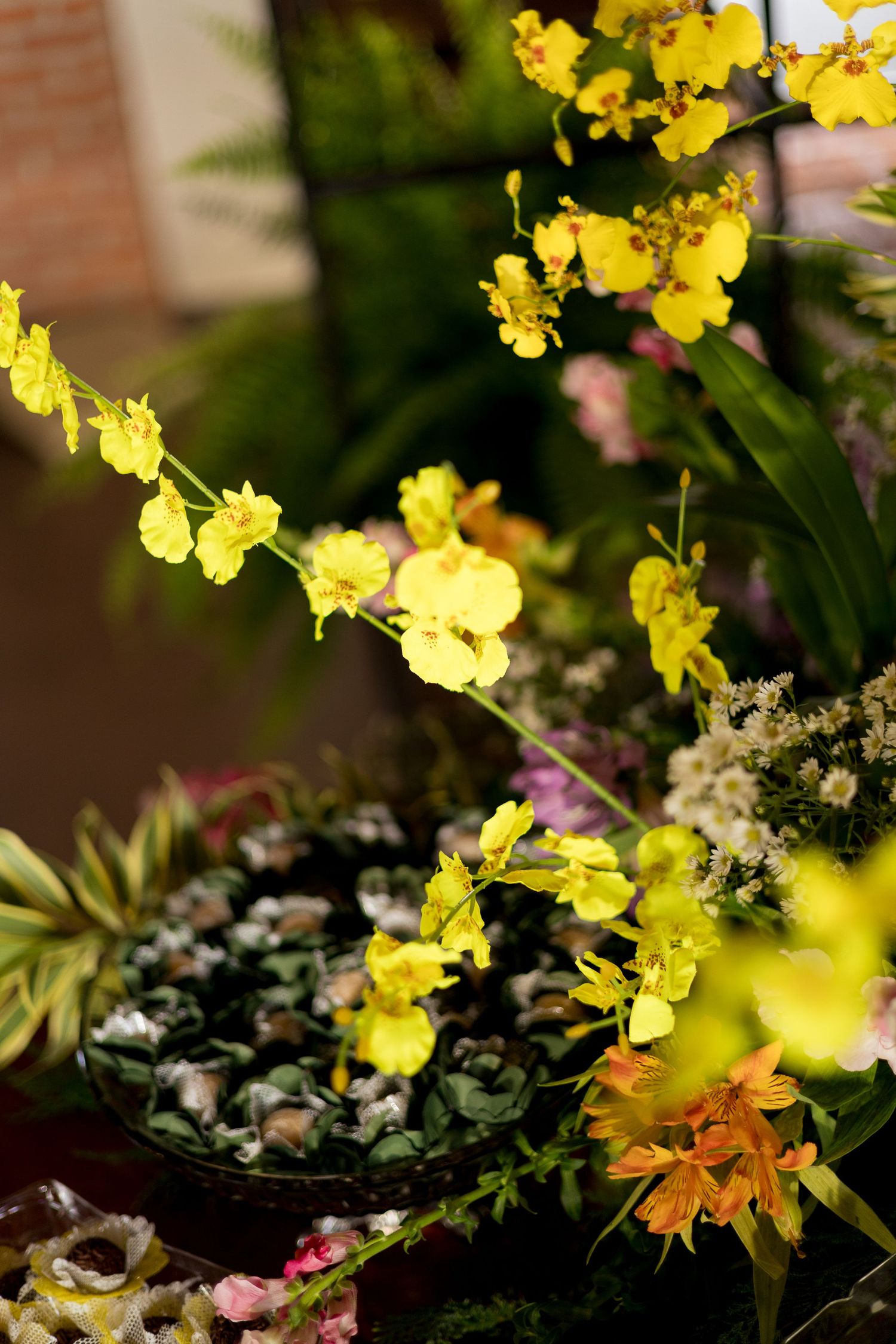 Vibrant yellow oncidium orchids cascade over a floral arrangement with mixed blooms and greenery in a garden setting.