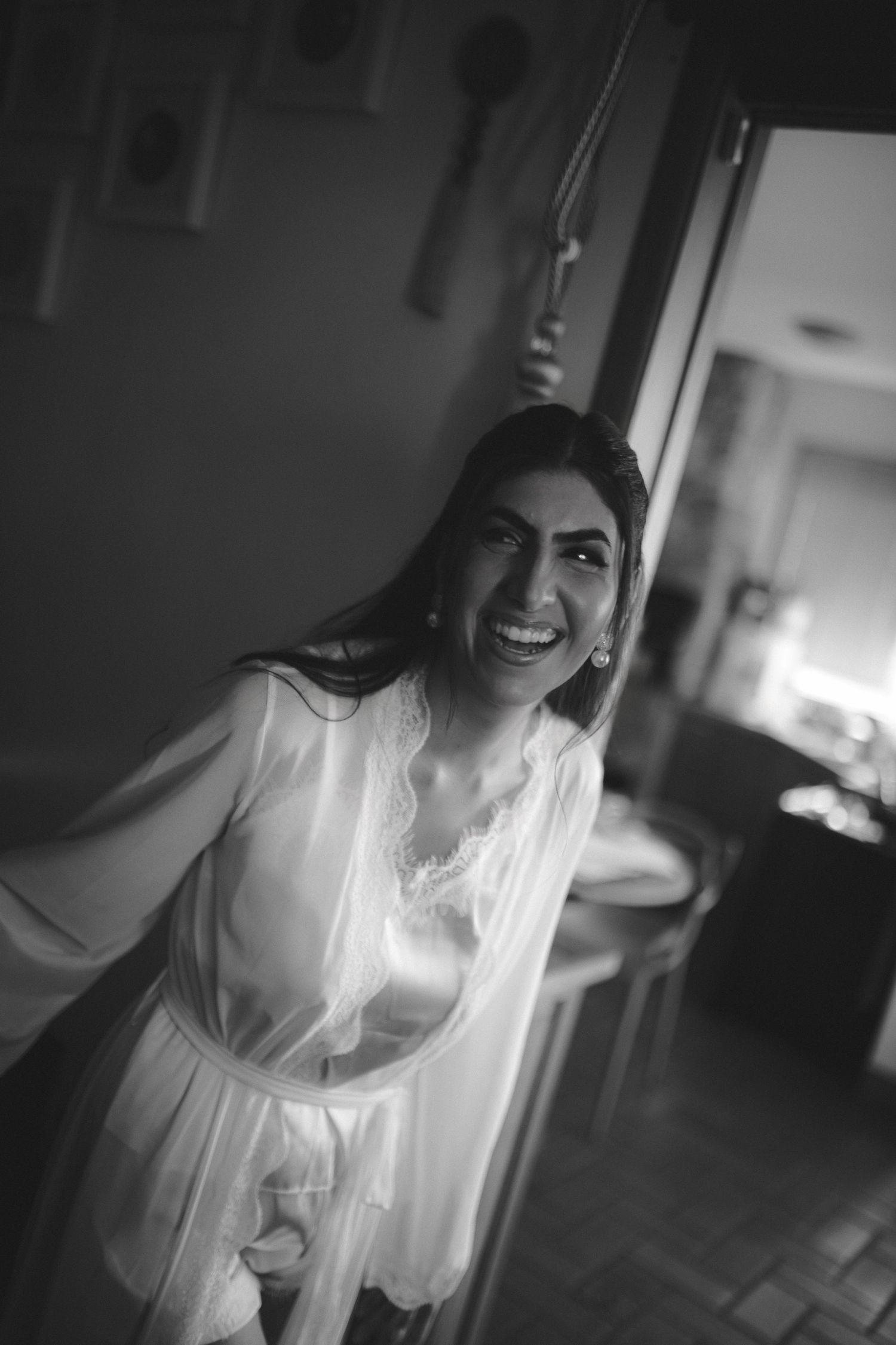 Black and white photo of a joyful woman in a lace robe laughing candidly indoors.