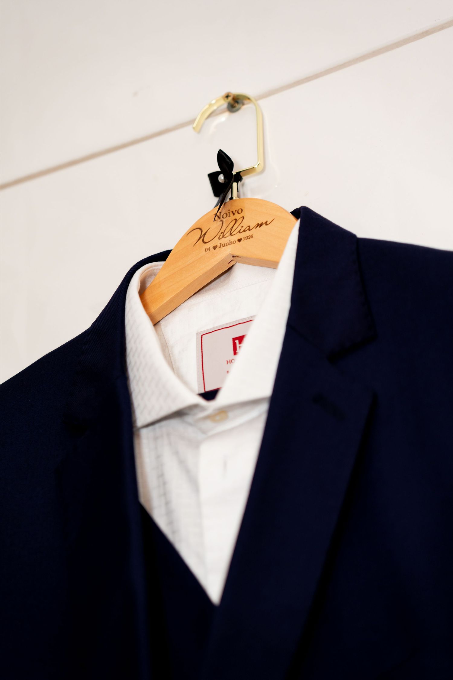 Navy blue suit jacket on a personalized wooden hanger with white dress shirt, displayed against a white wall.