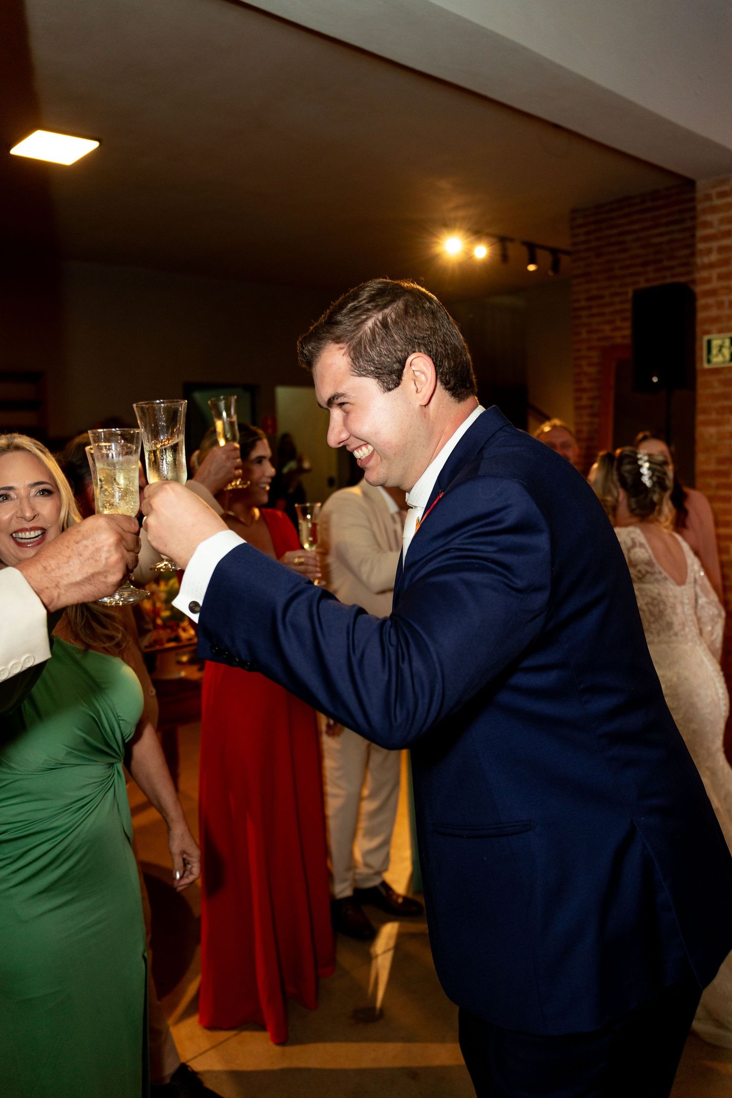 Groom in navy suit toasting champagne with guests at elegant wedding reception celebration.