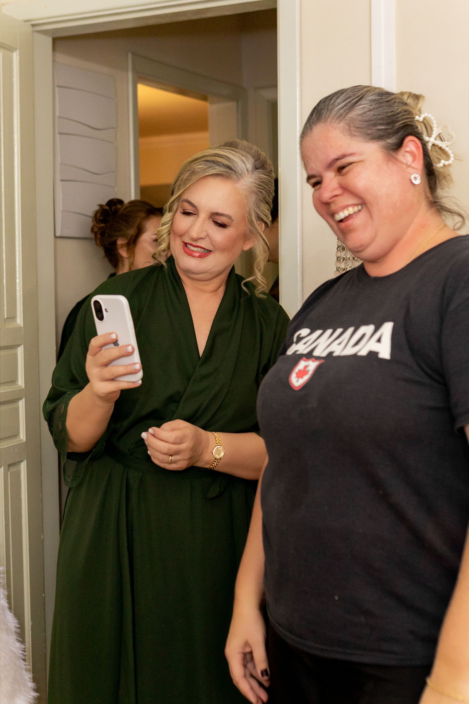 Two women smiling and looking at a phone, one wearing a green robe and one in a Canada t-shirt.