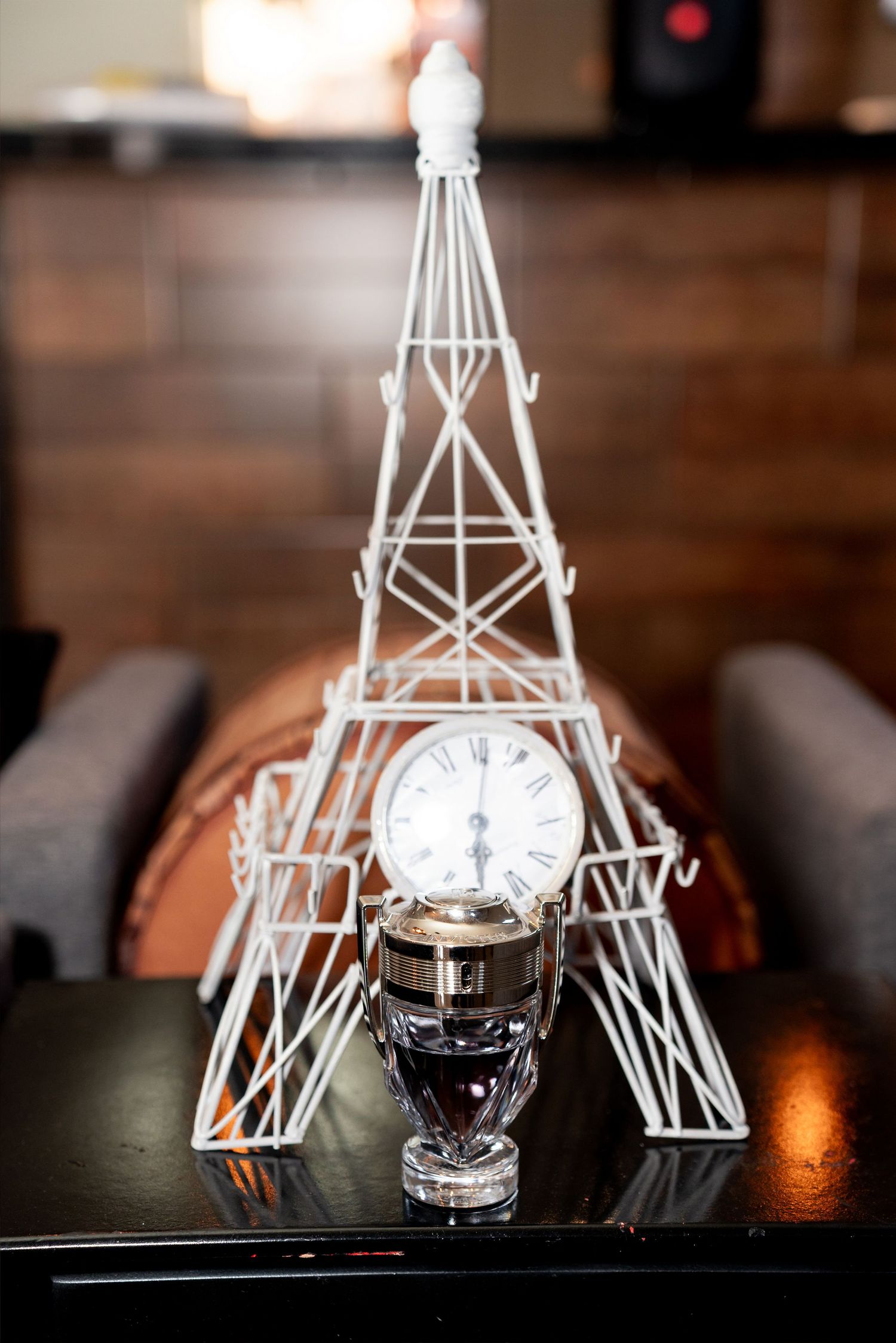 White wire Eiffel Tower decor with a vintage clock and crystal trophy on a black table.