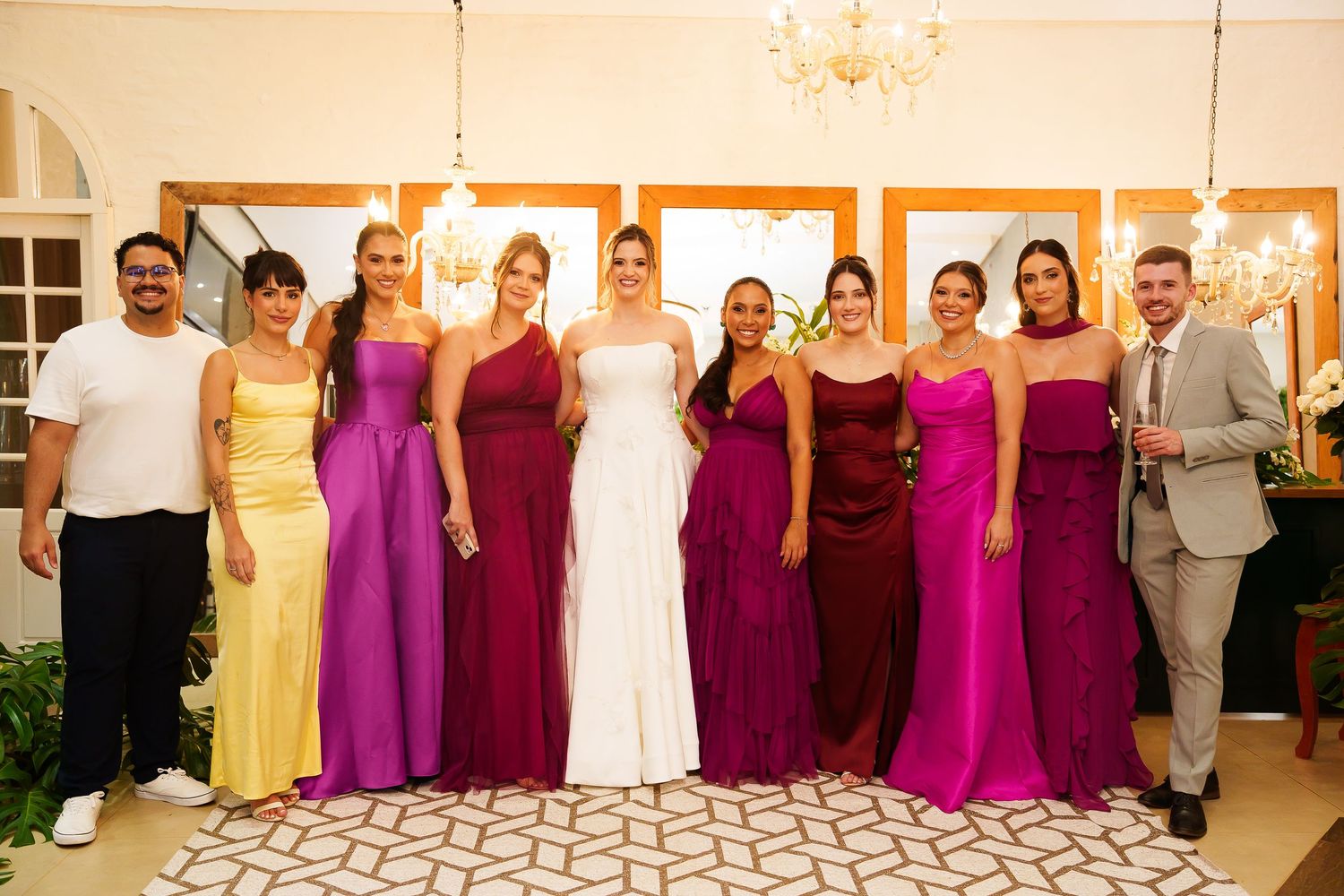 Bride in white gown poses with bridesmaids in colorful yellow, purple, and red dresses at an elegant wedding reception.