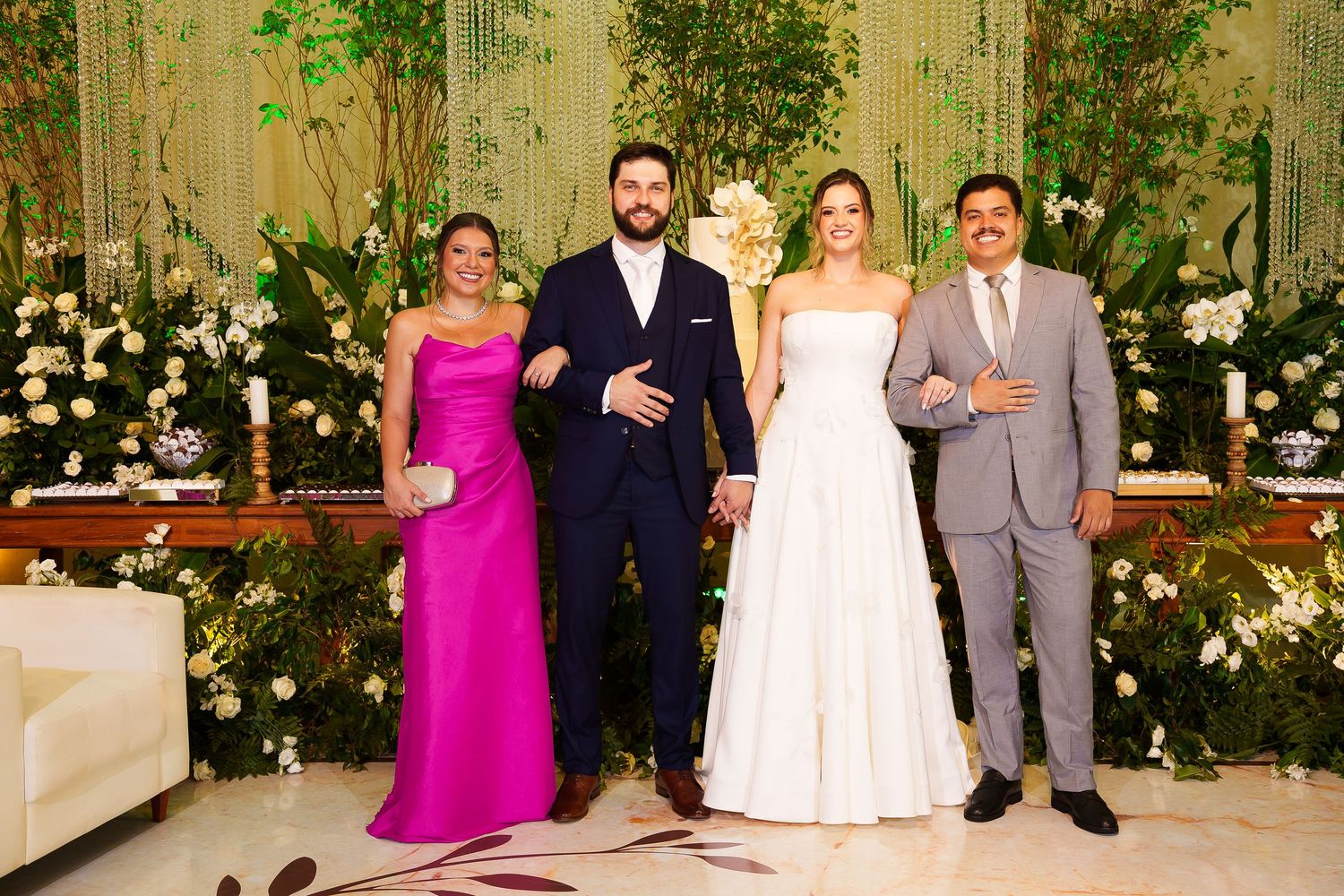 Wedding party of four posing elegantly, bride in white gown, groom in navy suit, guests in pink and gray formal attire.
