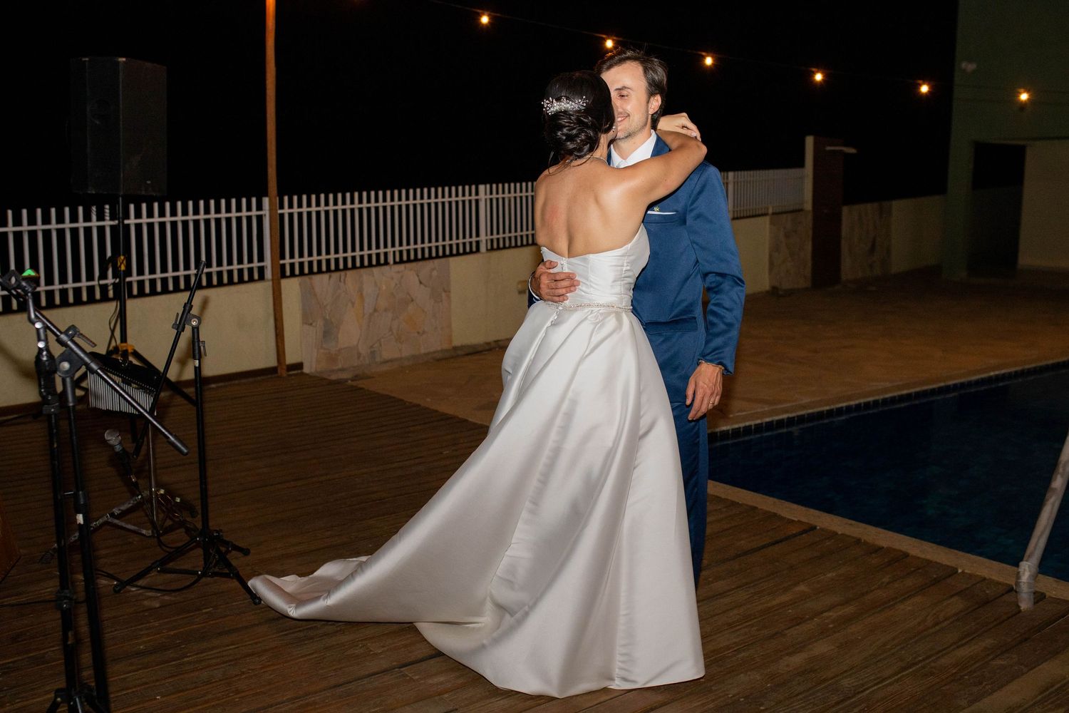 Bride and groom share their first dance outdoors at night near a pool during their wedding reception.