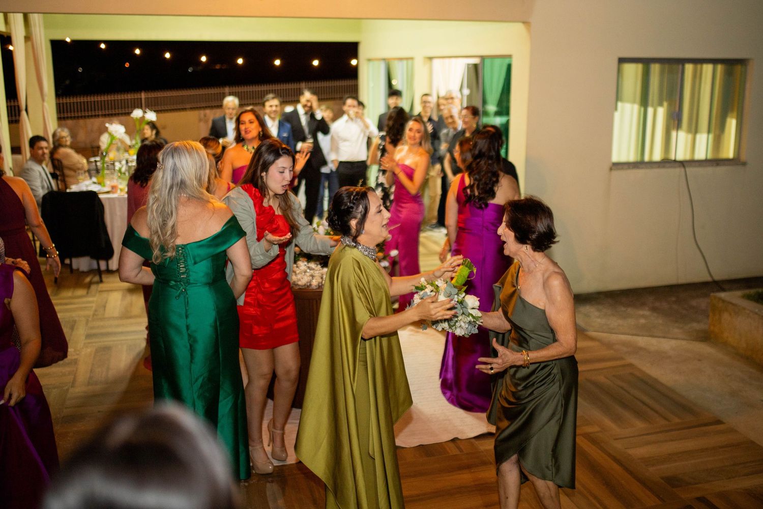 Guests mingling at a wedding reception, wearing colorful formal dresses in green, red, and purple hues.