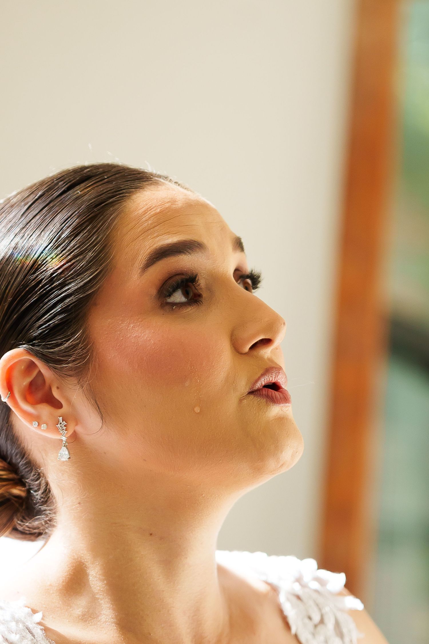 Close-up portrait of a bride in white lace dress with elegant updo and crystal drop earrings, gazing upward.
