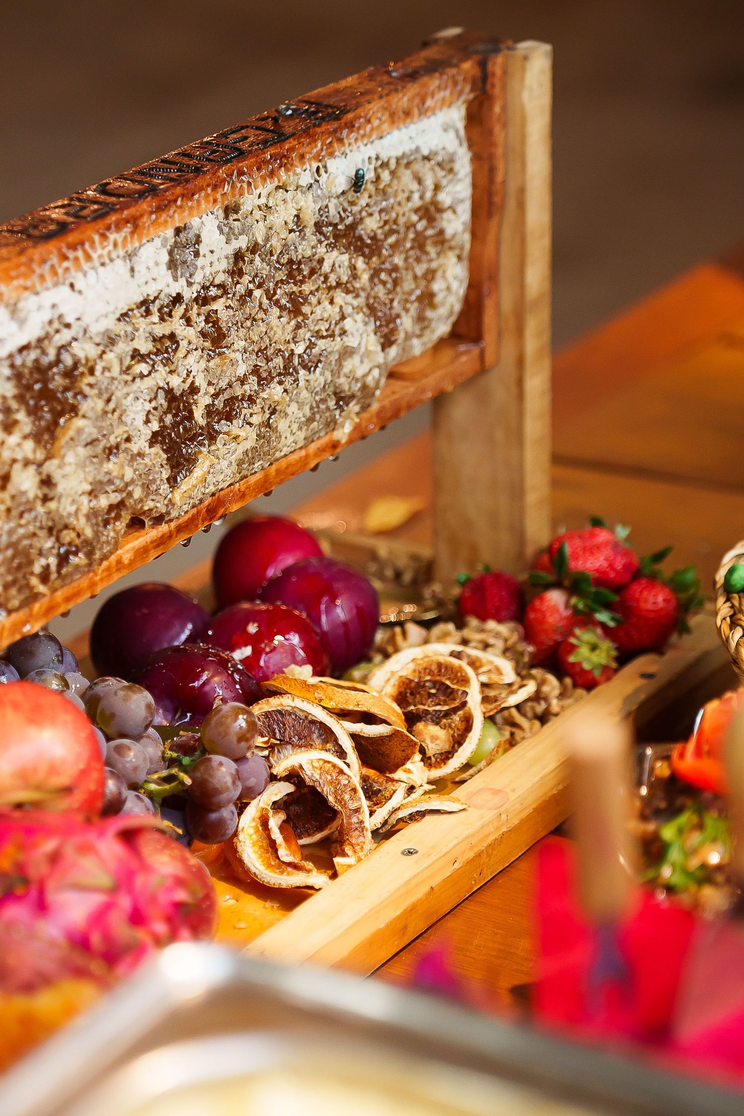 Wooden box filled with fresh fruits, dried citrus, grapes, strawberries, and honeycomb at a buffet display.