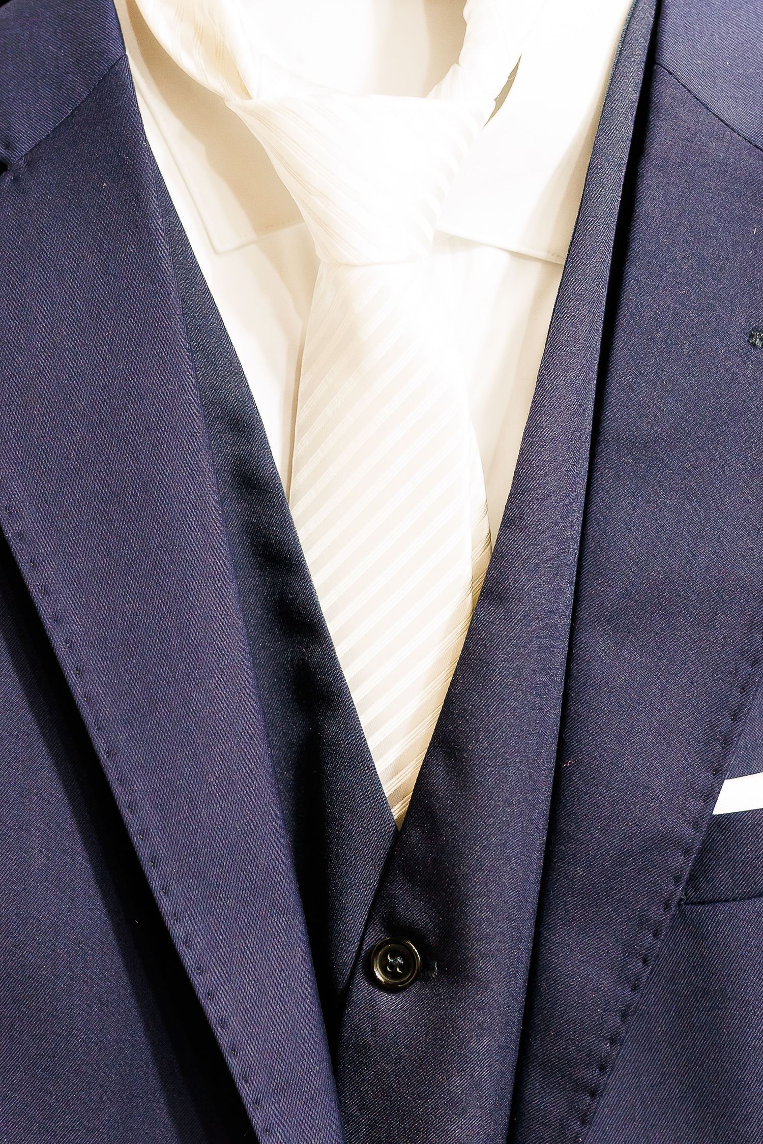 Navy blue three-piece suit with cream striped tie and white dress shirt, close-up formal menswear detail.
