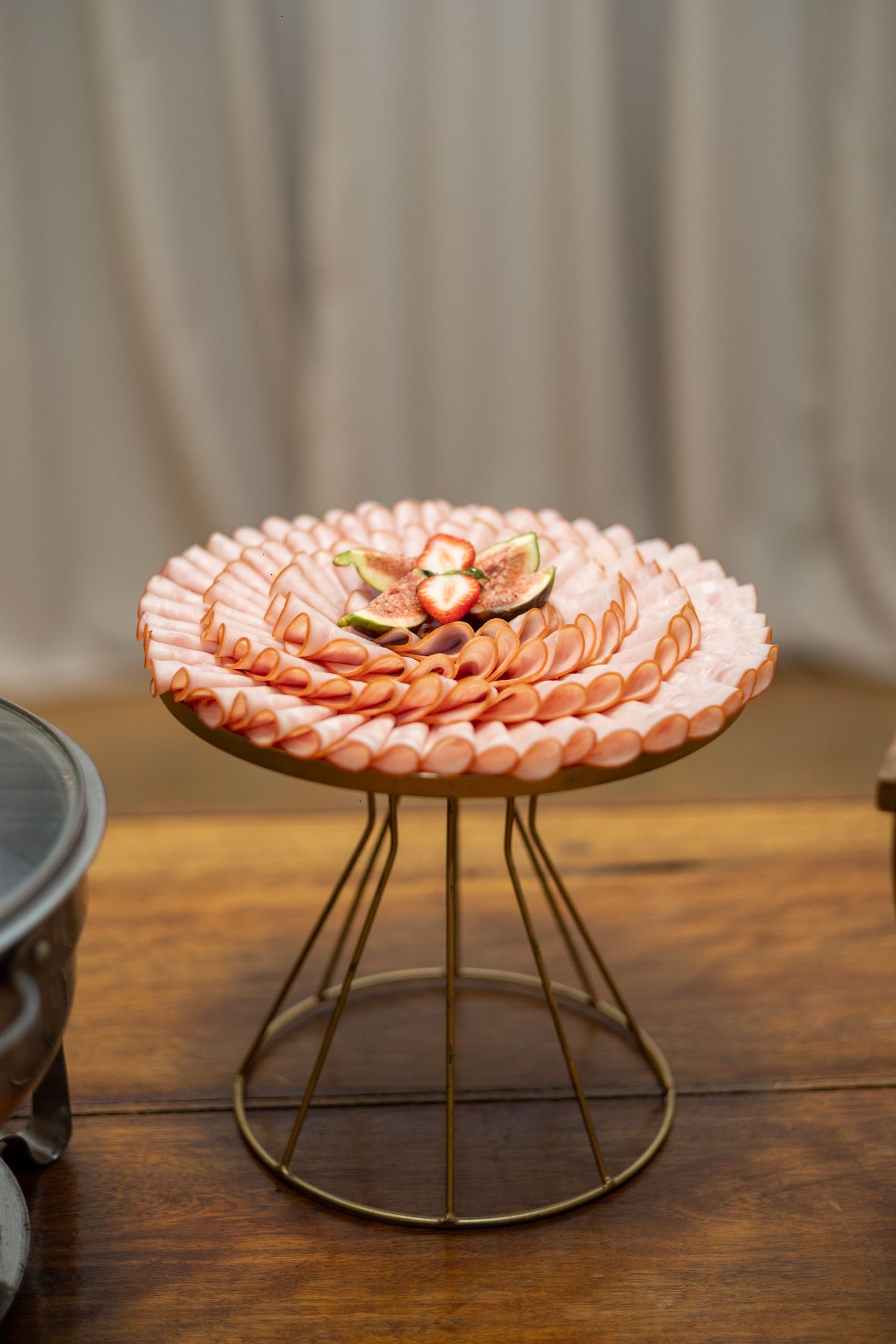 Elegant charcuterie platter with rolled deli meats and fresh figs displayed on a gold wire pedestal stand.