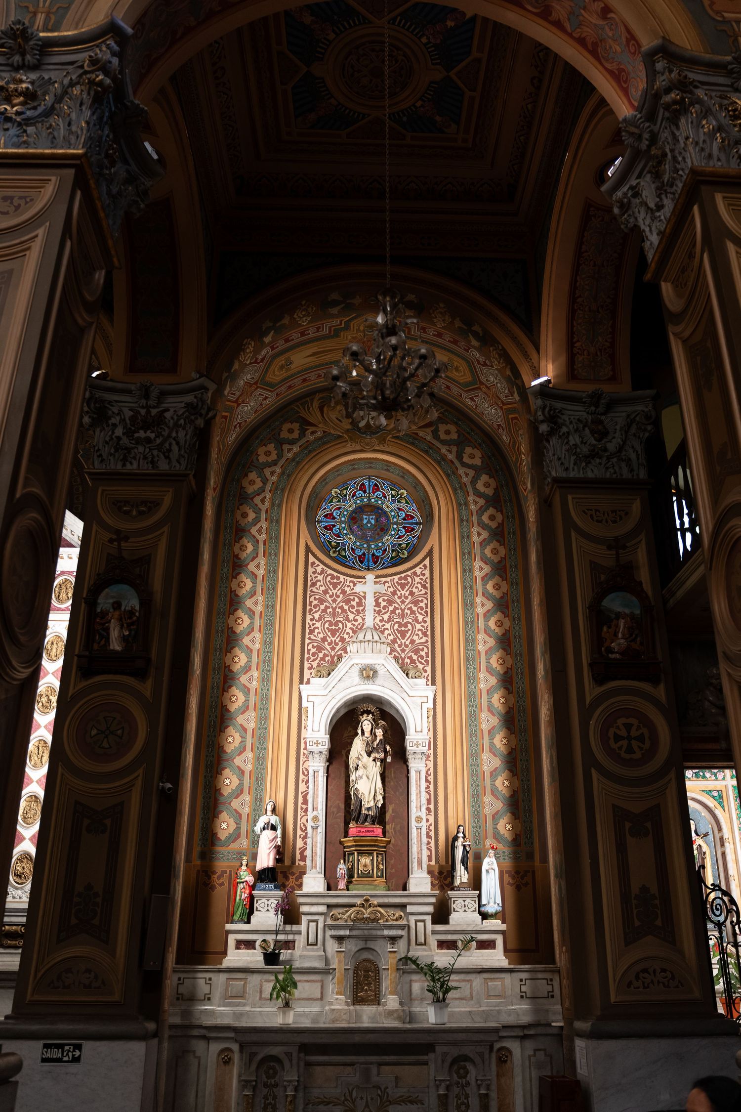 Ornate Catholic church interior featuring a gilded altar, religious statues, rose window, and richly decorated arched ceilings.