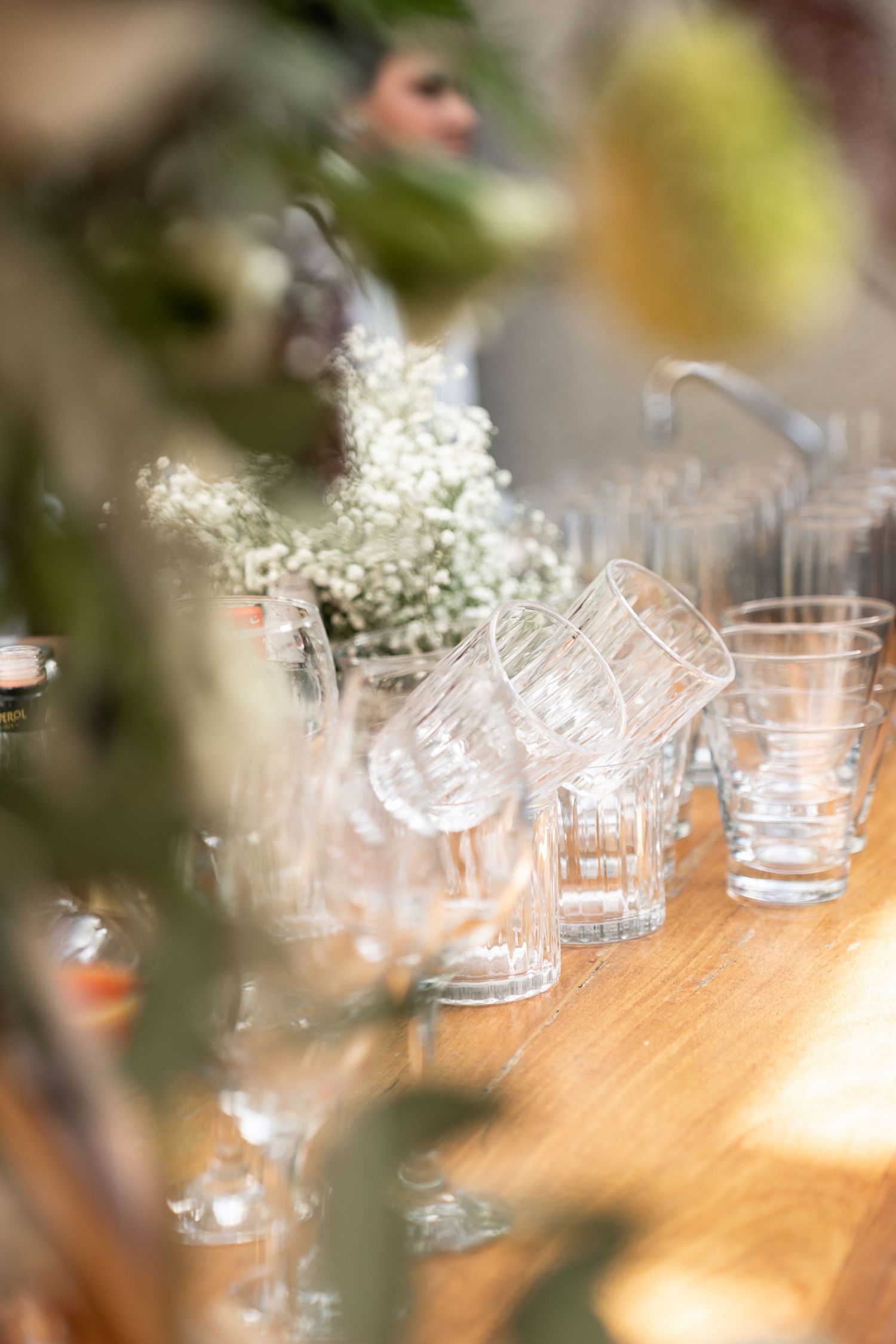 Clear glass tumblers arranged on a wooden table with white baby's breath flowers at an elegant event setting.