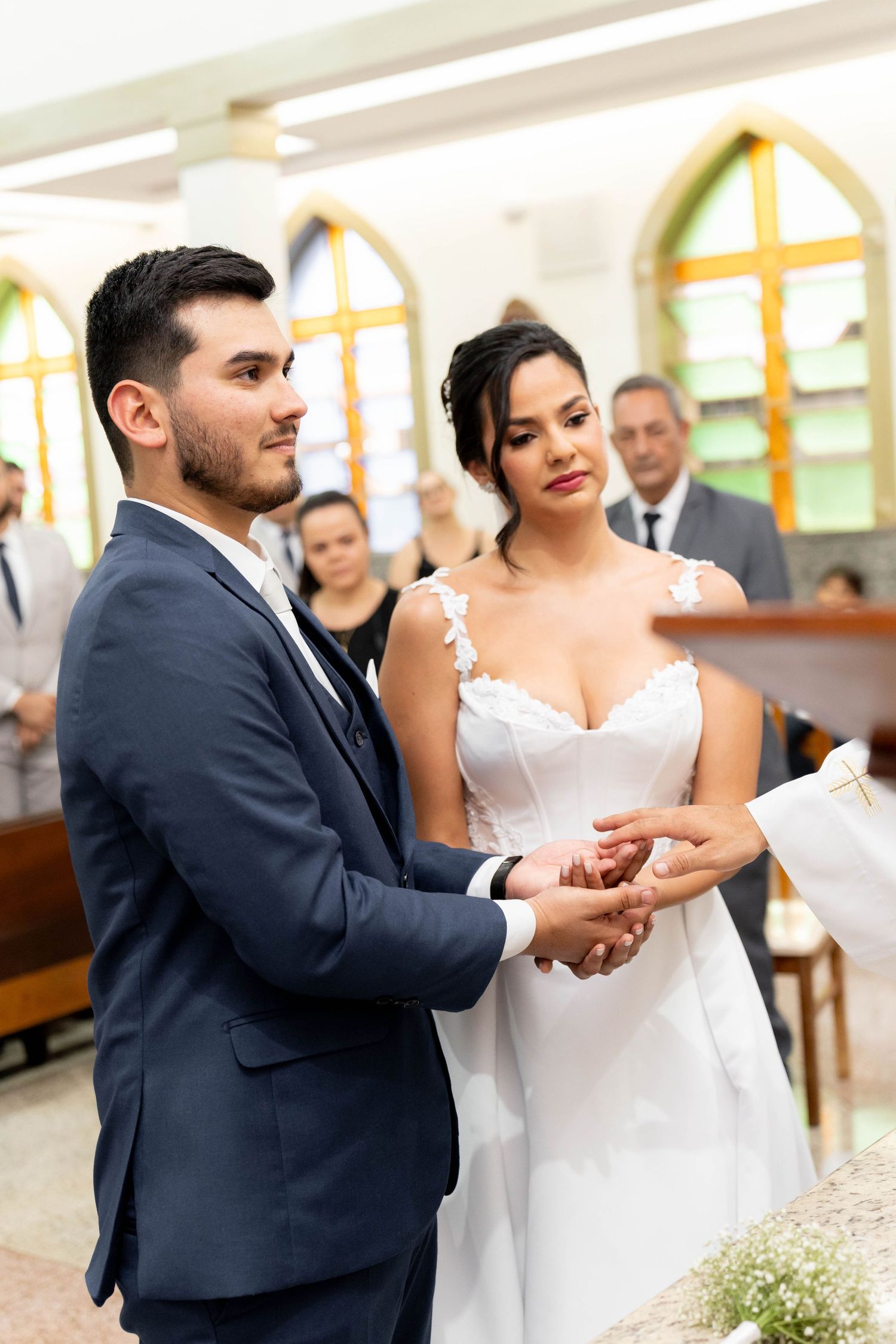 Bride and groom exchange rings during a church wedding ceremony, with guests seated in pews behind them.