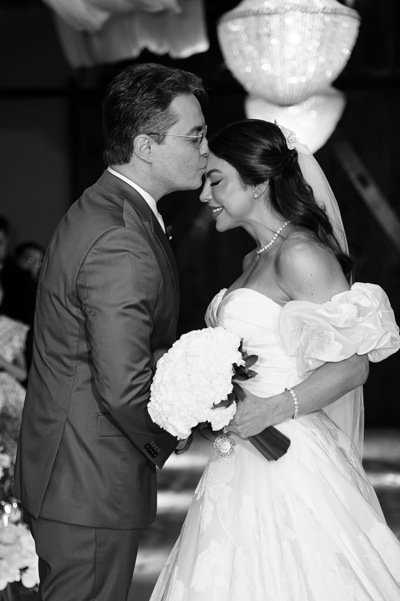 Black and white wedding photo of bride and groom sharing a tender moment, bride holding white bouquet in elegant ballgown.