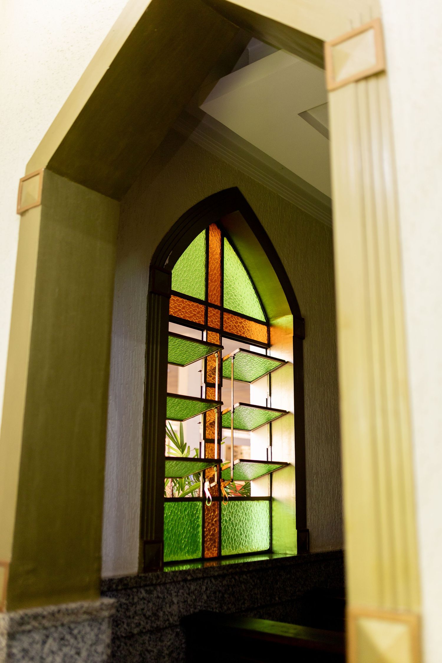 Gothic arched stained glass window with green and amber panels in a church alcove.
