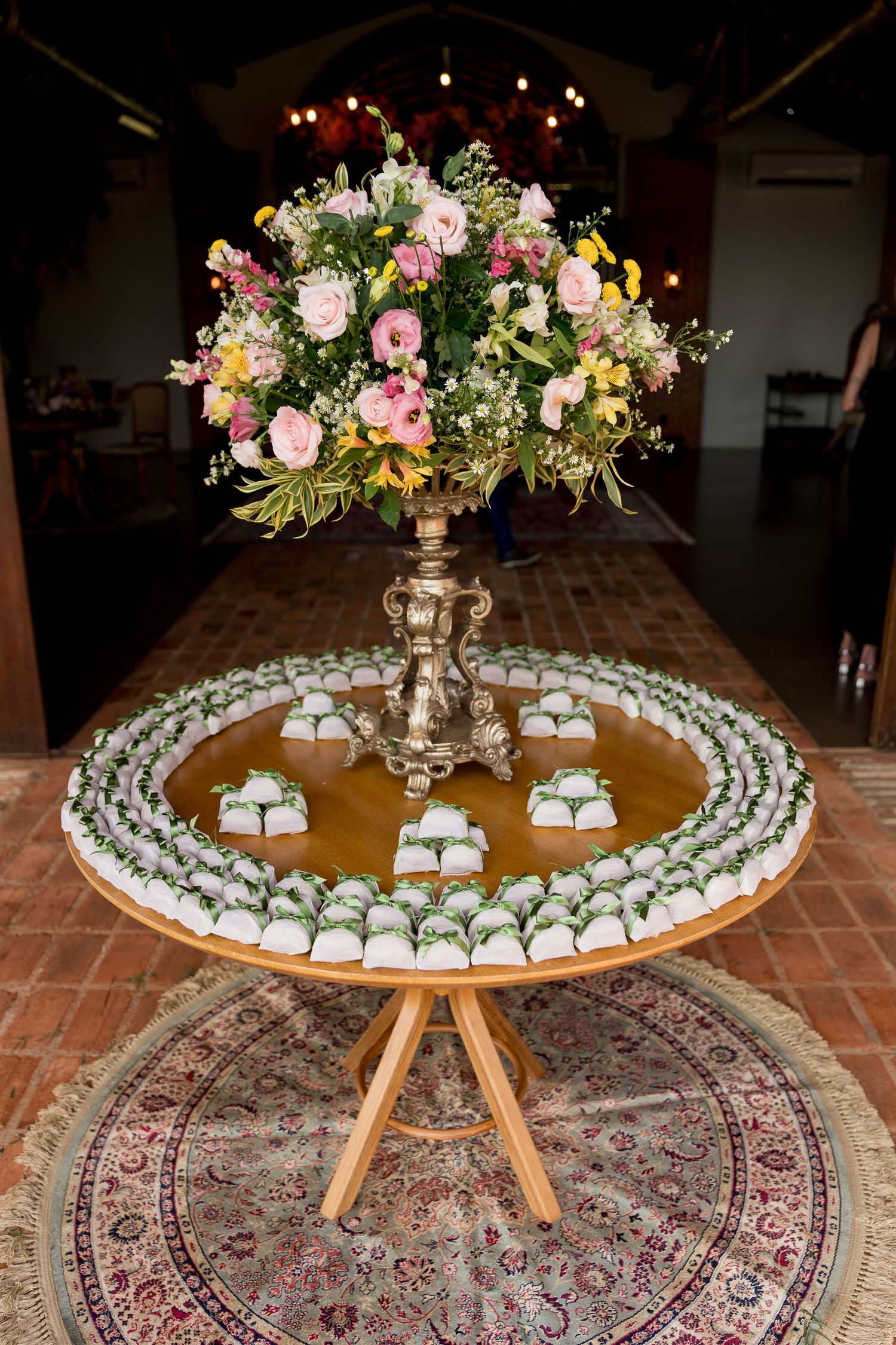 Elegant wedding dessert table with white treats arranged in circles around a gold vase holding a lush pink and yellow floral arrangement.