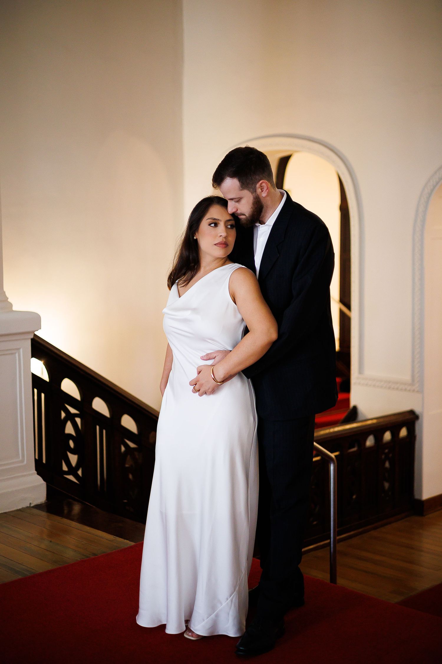 Elegant couple in wedding attire embracing on red carpet staircase in a classic venue.