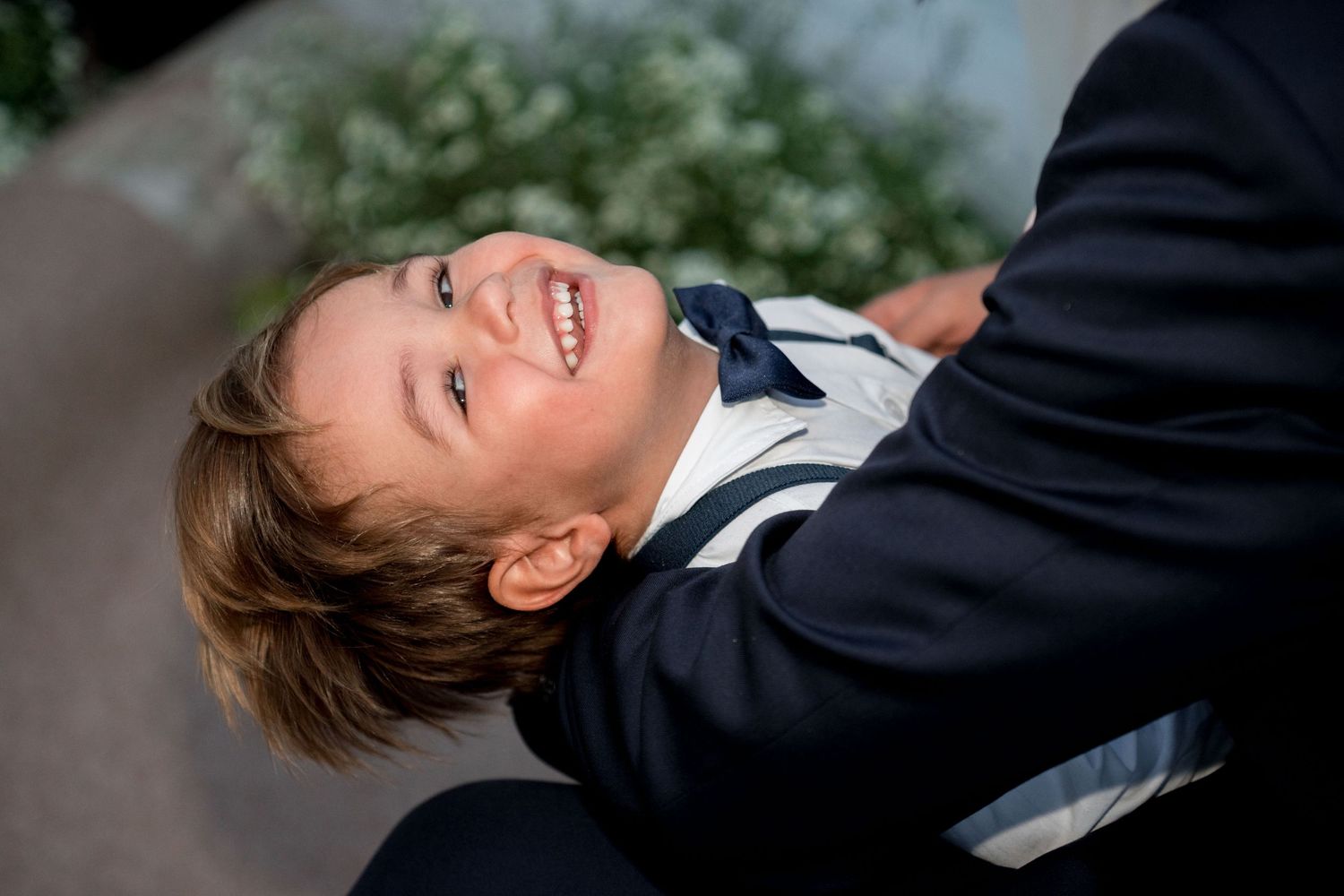 Smiling young boy in formal suit looks up happily at a wedding celebration outdoors.