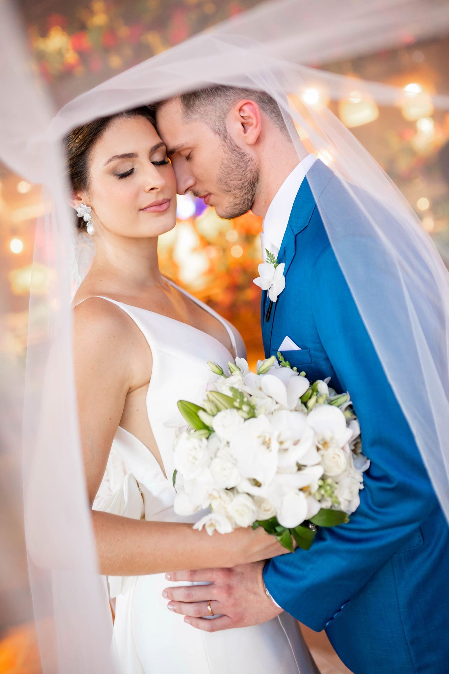Bride and groom share an intimate moment under a veil, surrounded by warm bokeh lights at their wedding.