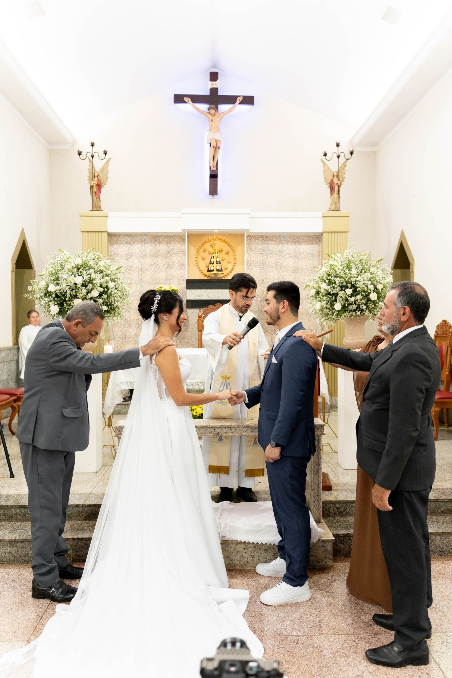 Bride and groom exchange vows at a Catholic church altar, flanked by family members during a traditional wedding ceremony.