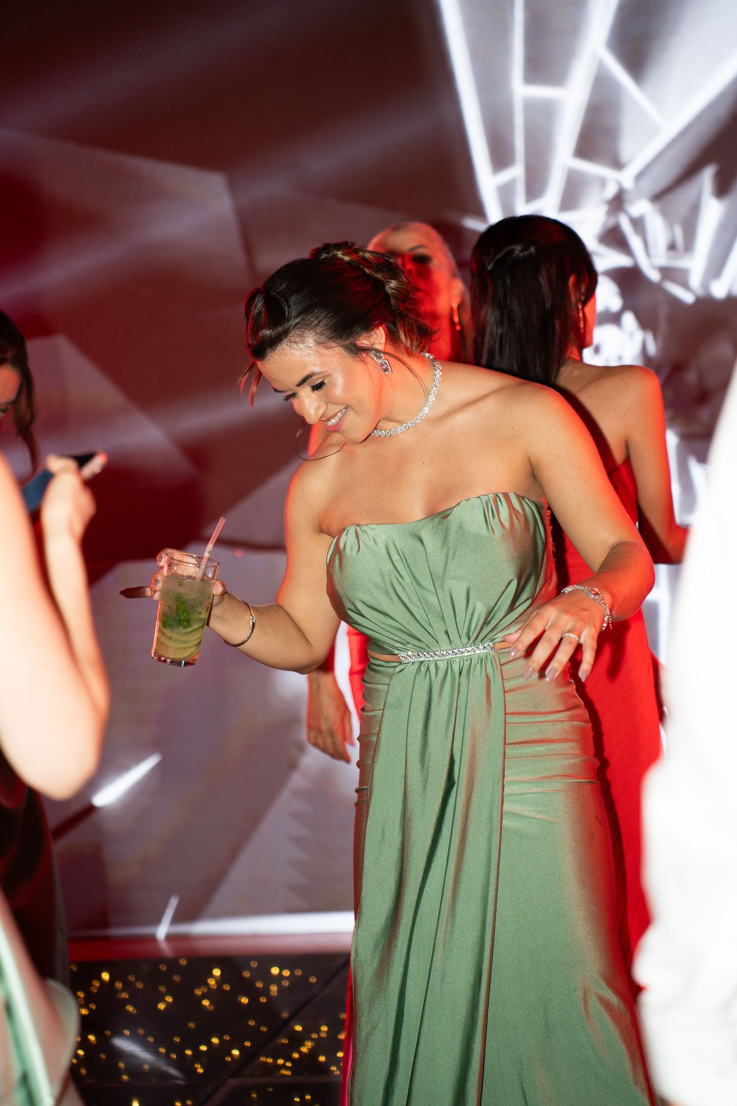 Woman in green strapless gown holding cocktail at elegant evening party event.