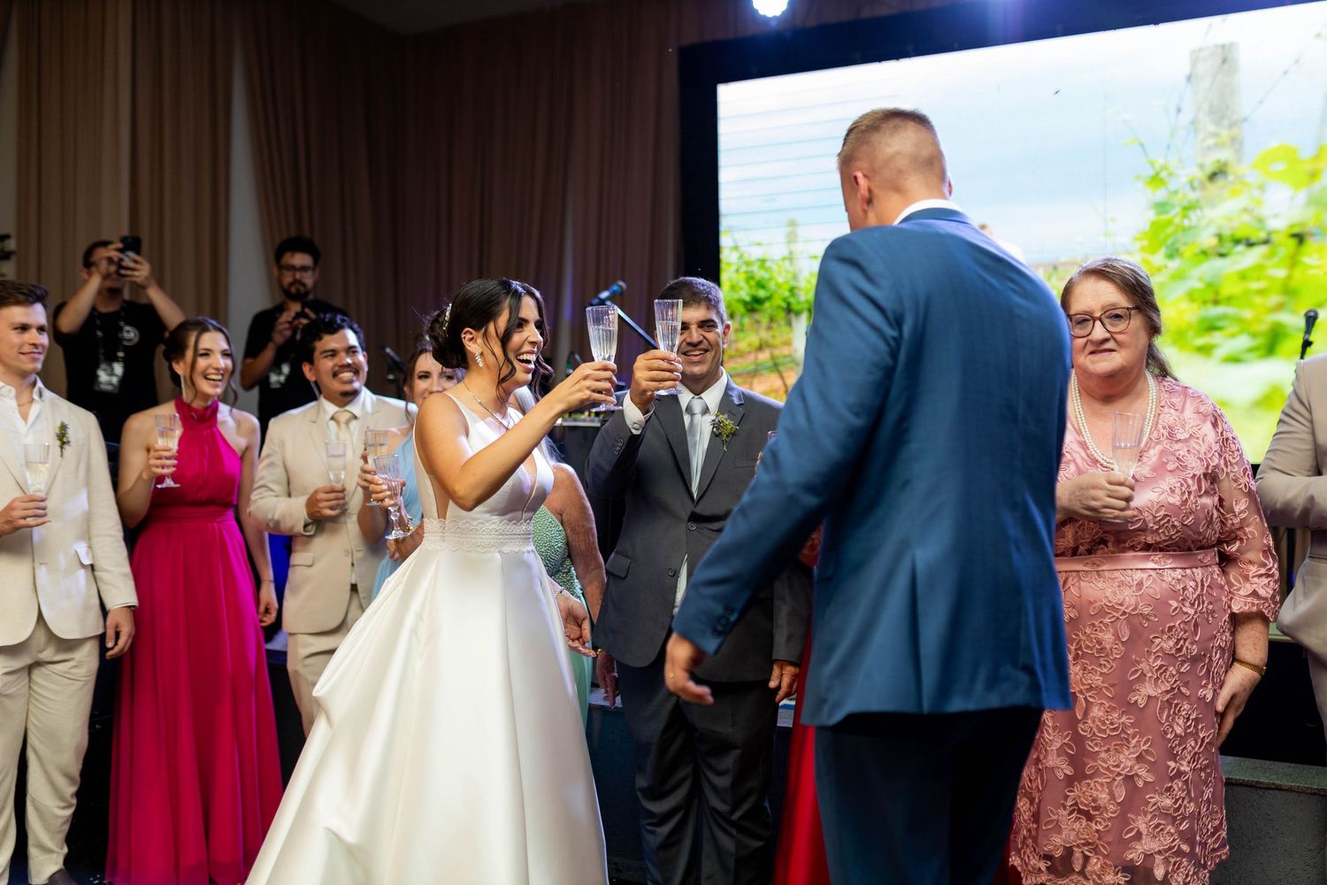 Bride and groom toasting with champagne glasses at wedding reception surrounded by guests in formal attire.
