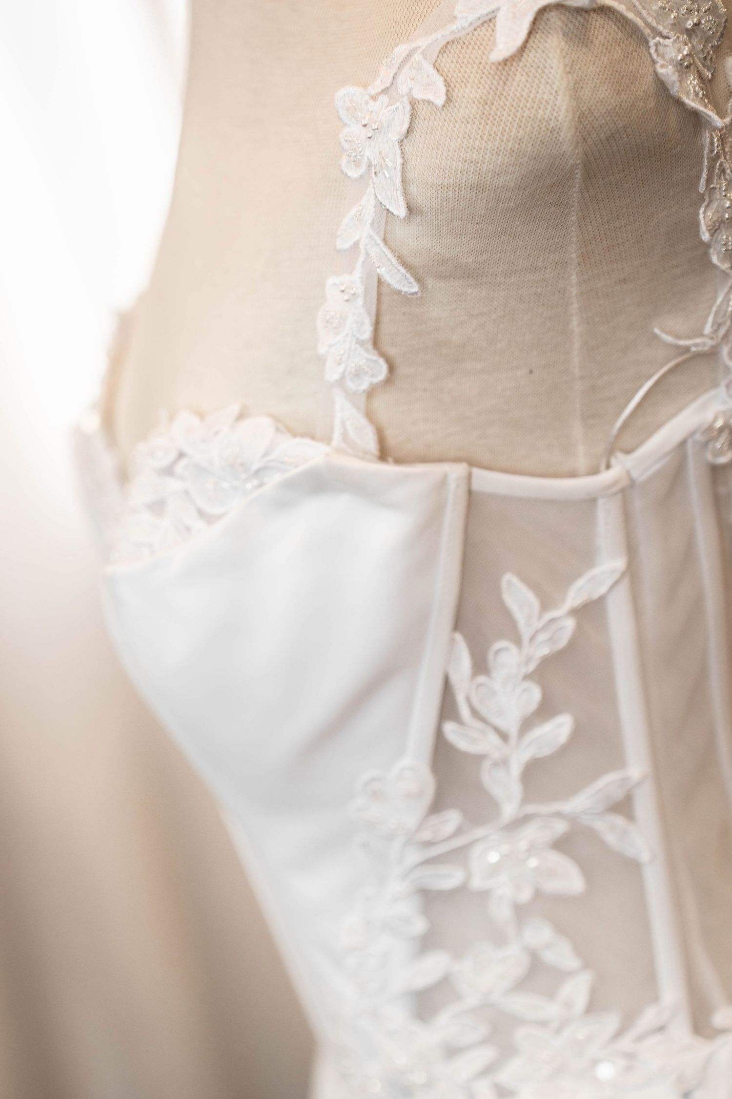 Close-up of an elegant white wedding dress with delicate floral lace detailing on a dressmaker mannequin.