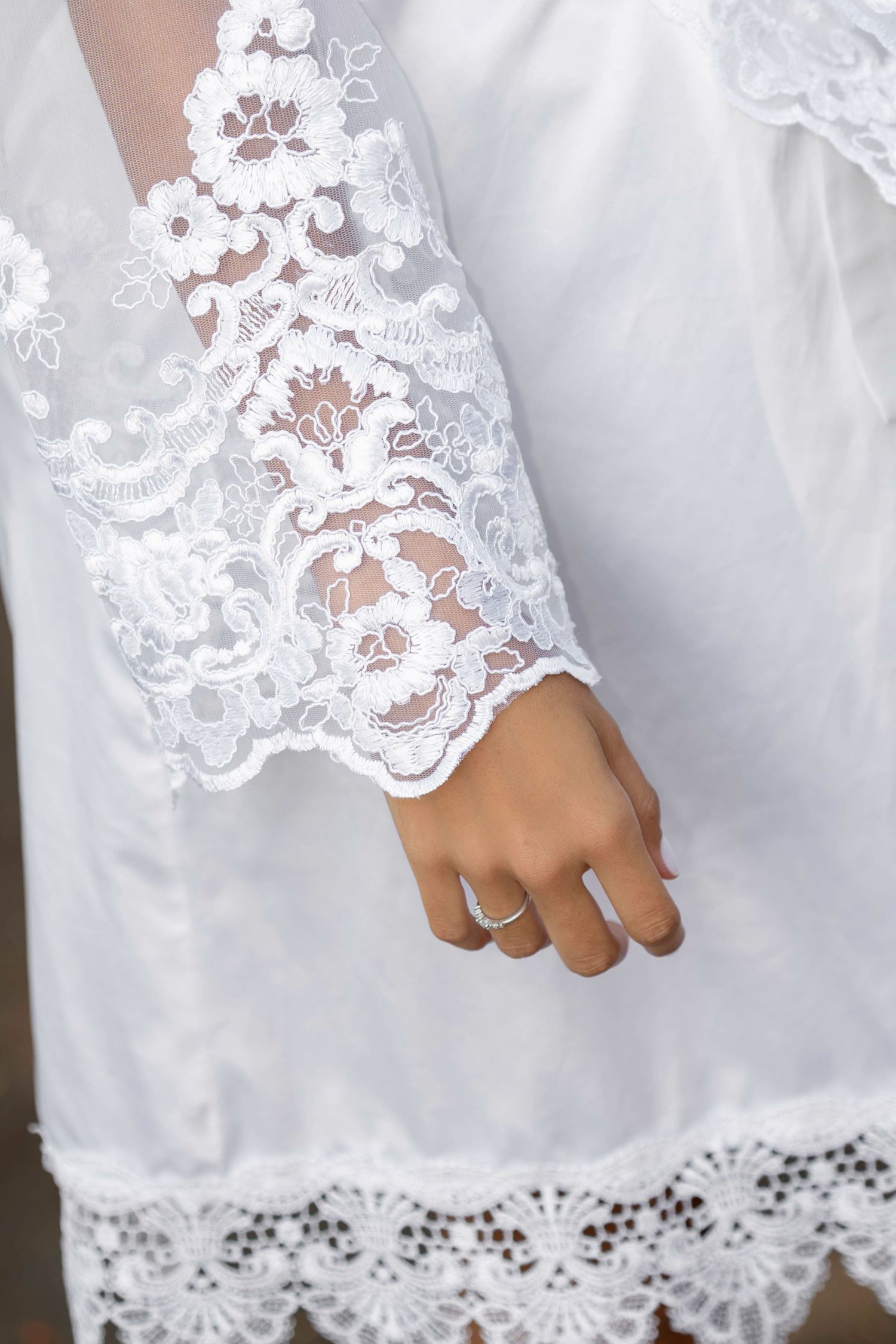 Close-up of a bride's hand wearing a ring, with elegant white lace sleeve detail on a wedding dress.