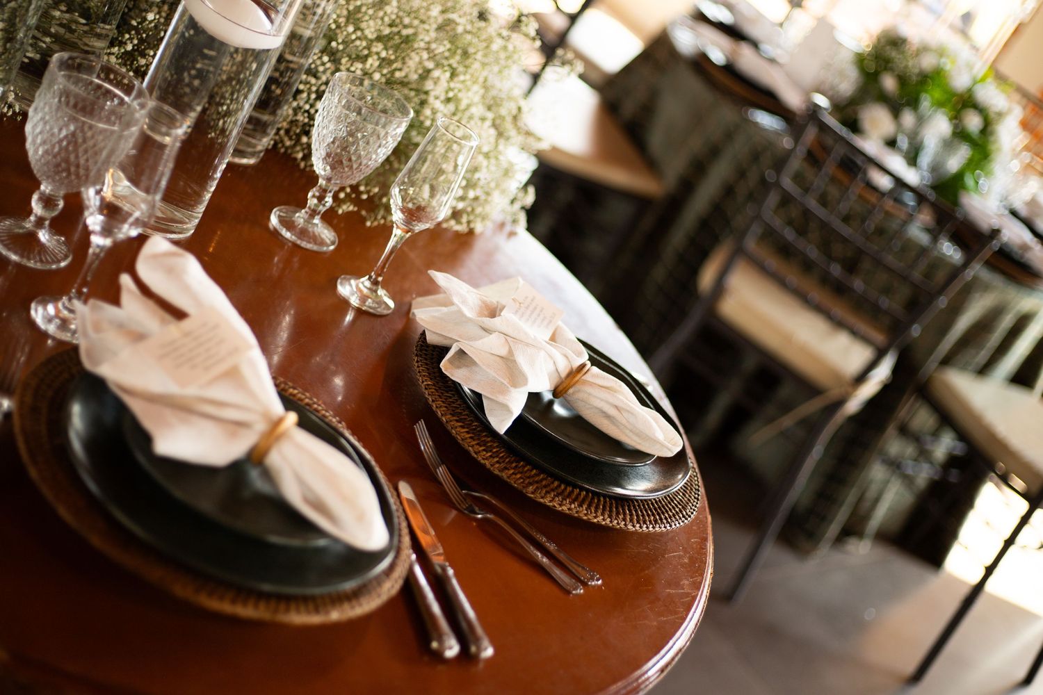 Elegant table setting with folded napkins, crystal glasses, and baby's breath floral centerpiece on a wooden dining table.