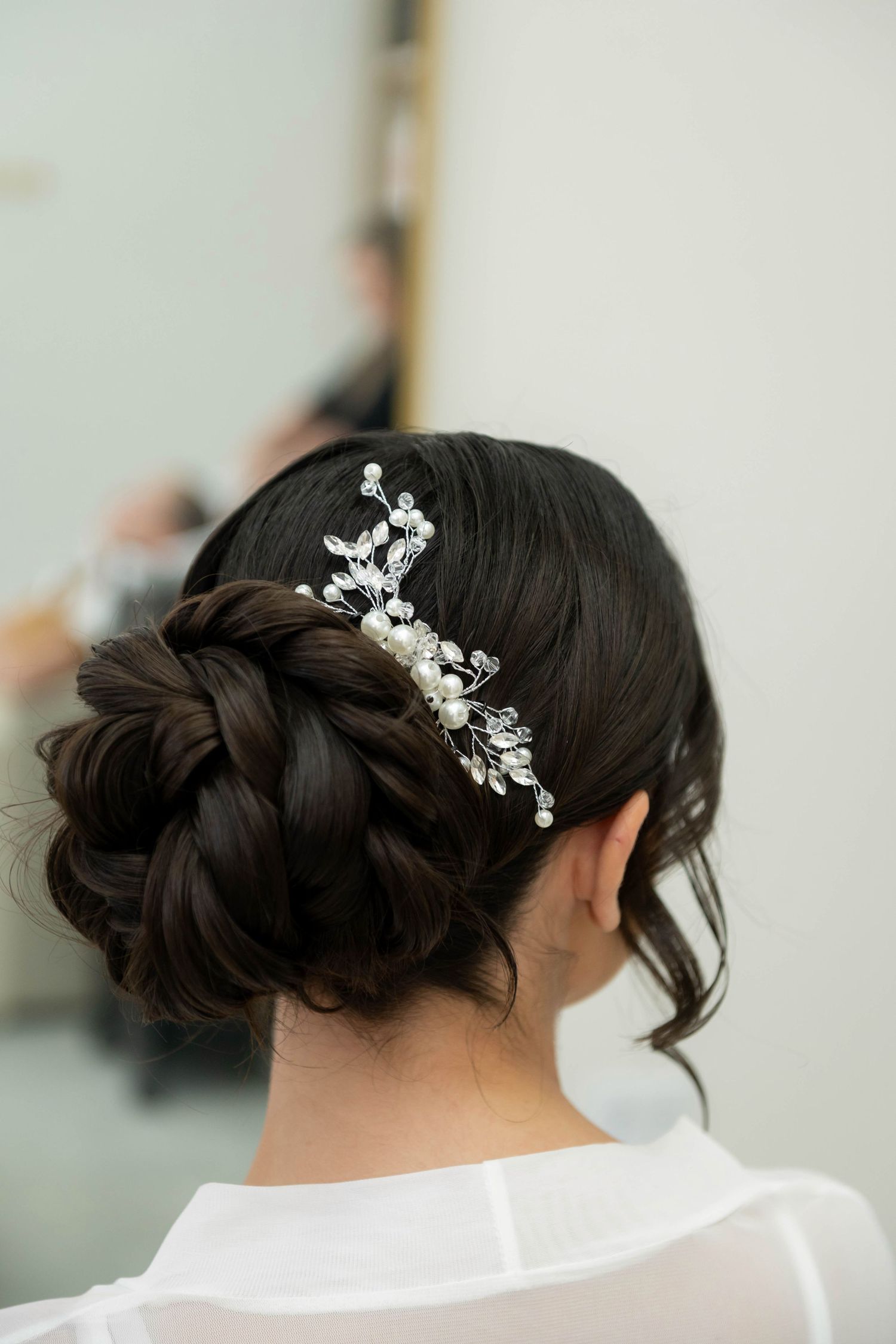 Elegant bridal updo with braided bun adorned with pearl and crystal hair comb, viewed from behind.