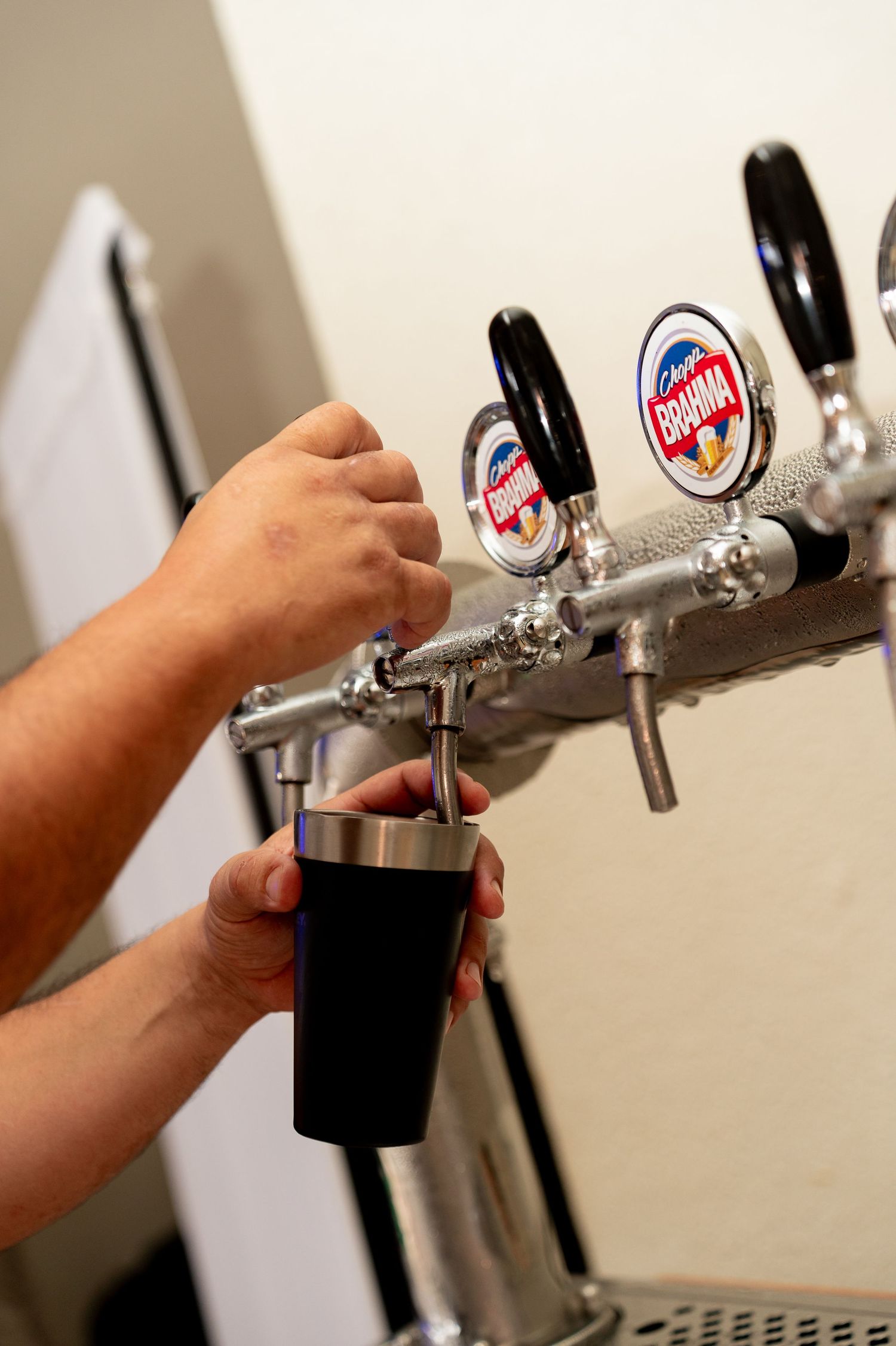 Bartender pouring dark beer from Brahma tap handles into a black cup at a bar.