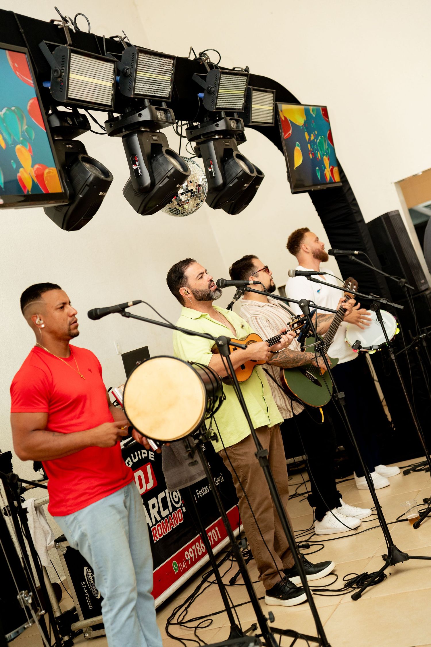 Live band performing on stage with guitars, drums, microphones, and colorful LED screens in the background.