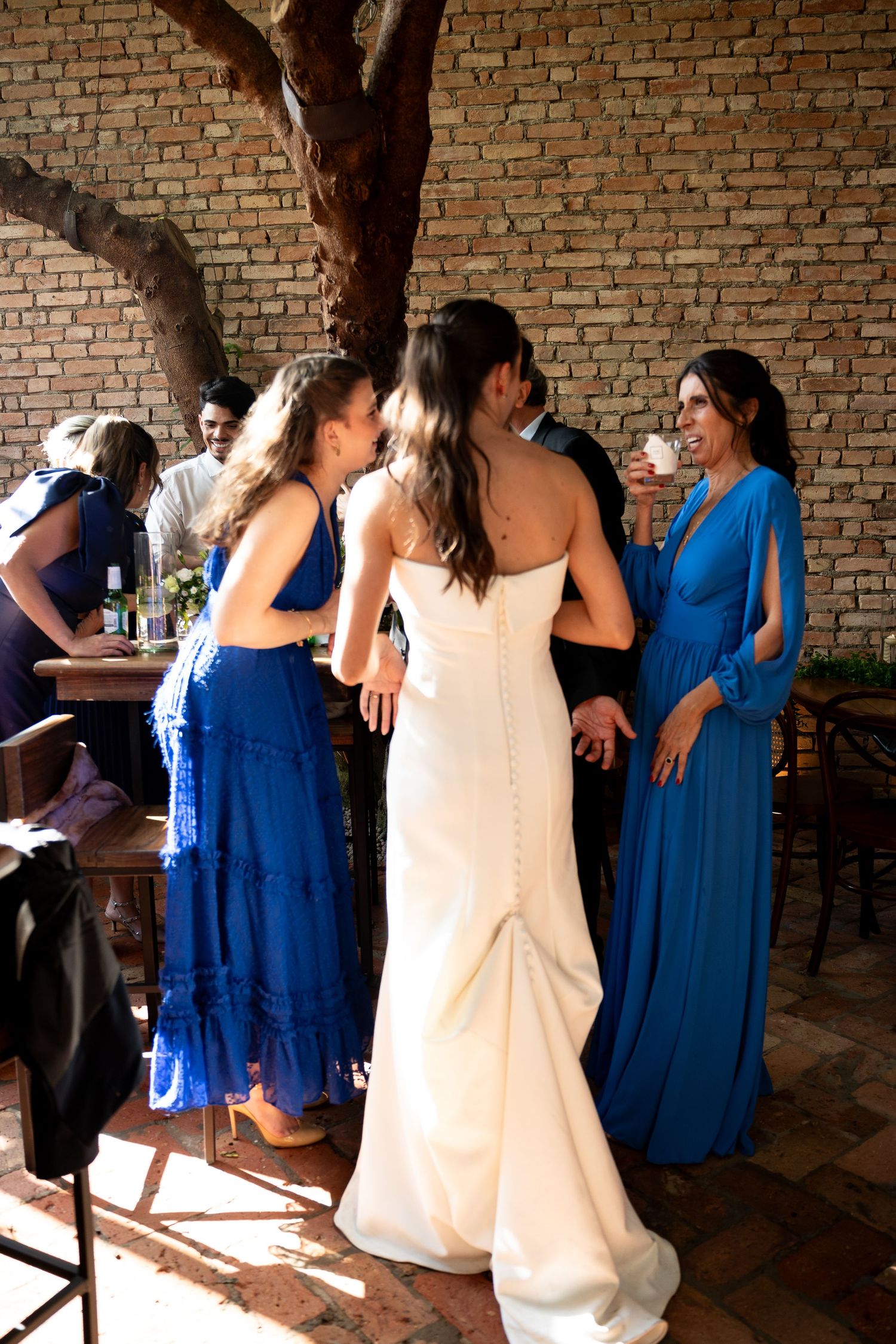 Bride in white gown with bridesmaids in blue dresses conversing at an outdoor wedding reception.