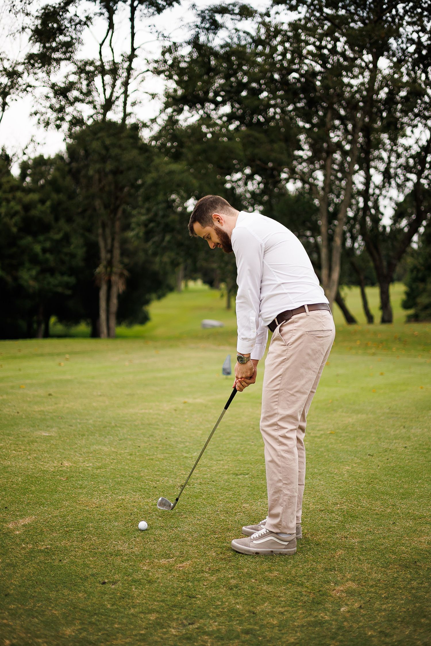 Man in white shirt and khaki pants preparing to swing a golf club on a lush green golf course.