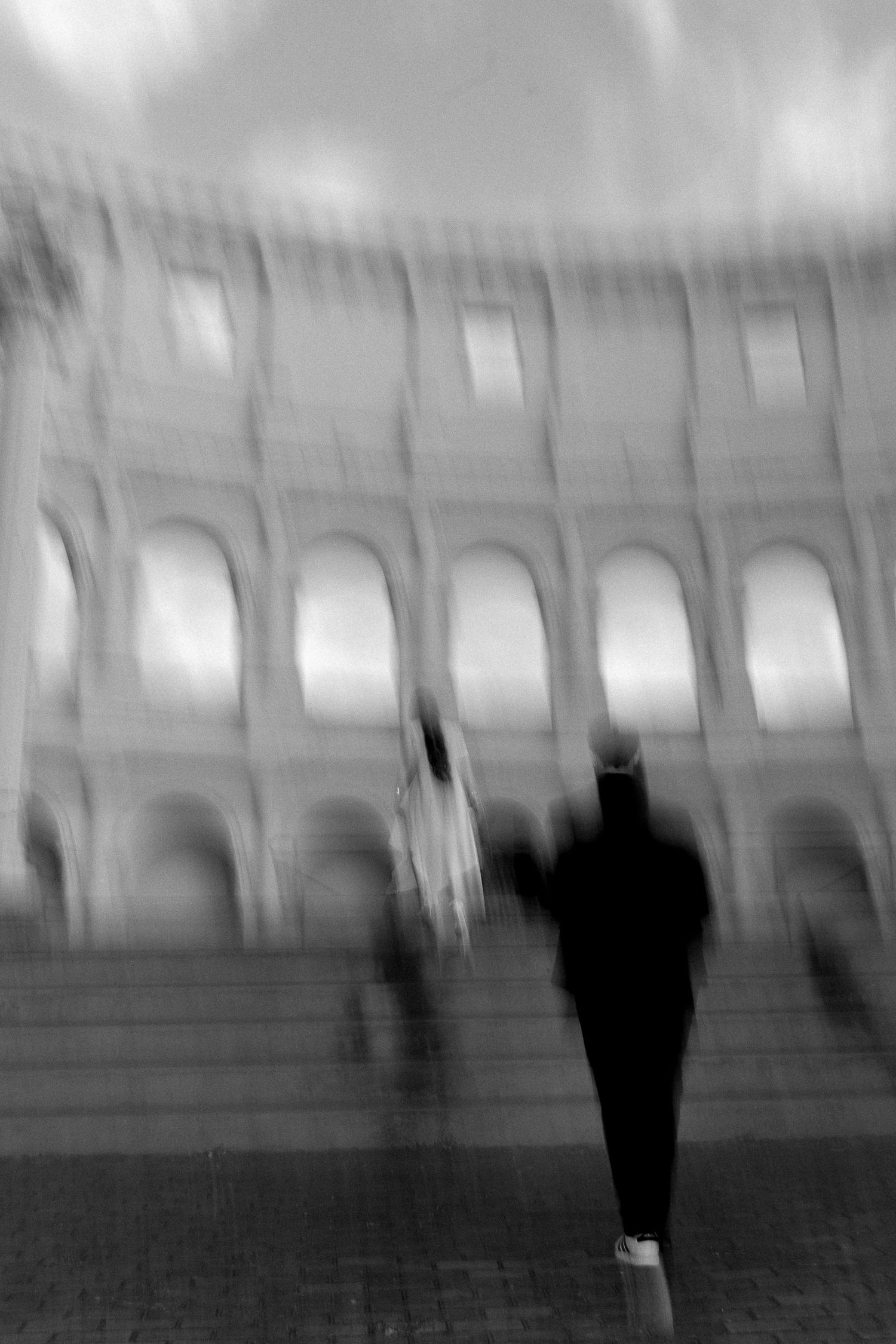 Blurry black and white photo of people walking in front of the Colosseum in Rome, Italy.