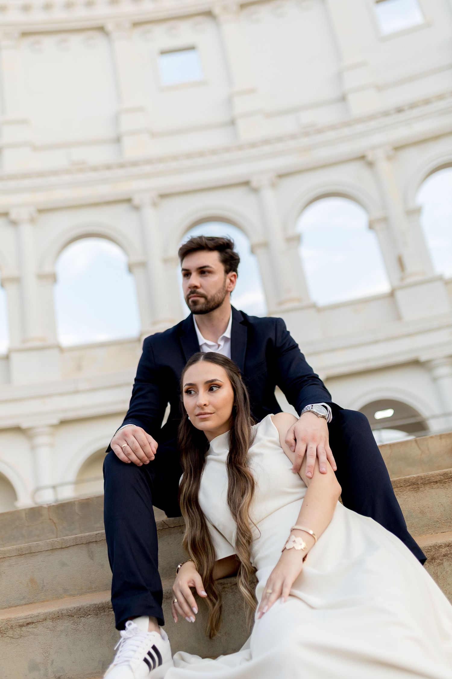 Elegant couple posing on steps in front of the Colosseum in Rome, Italy, wearing stylish formal attire.