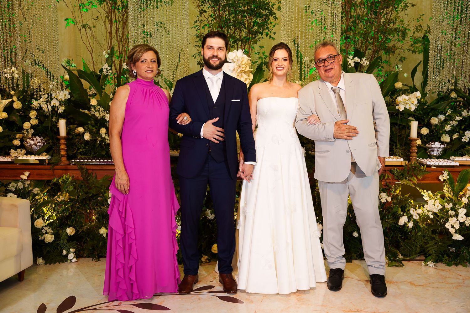 A bride and groom pose with family members at an elegant wedding reception with floral decorations.