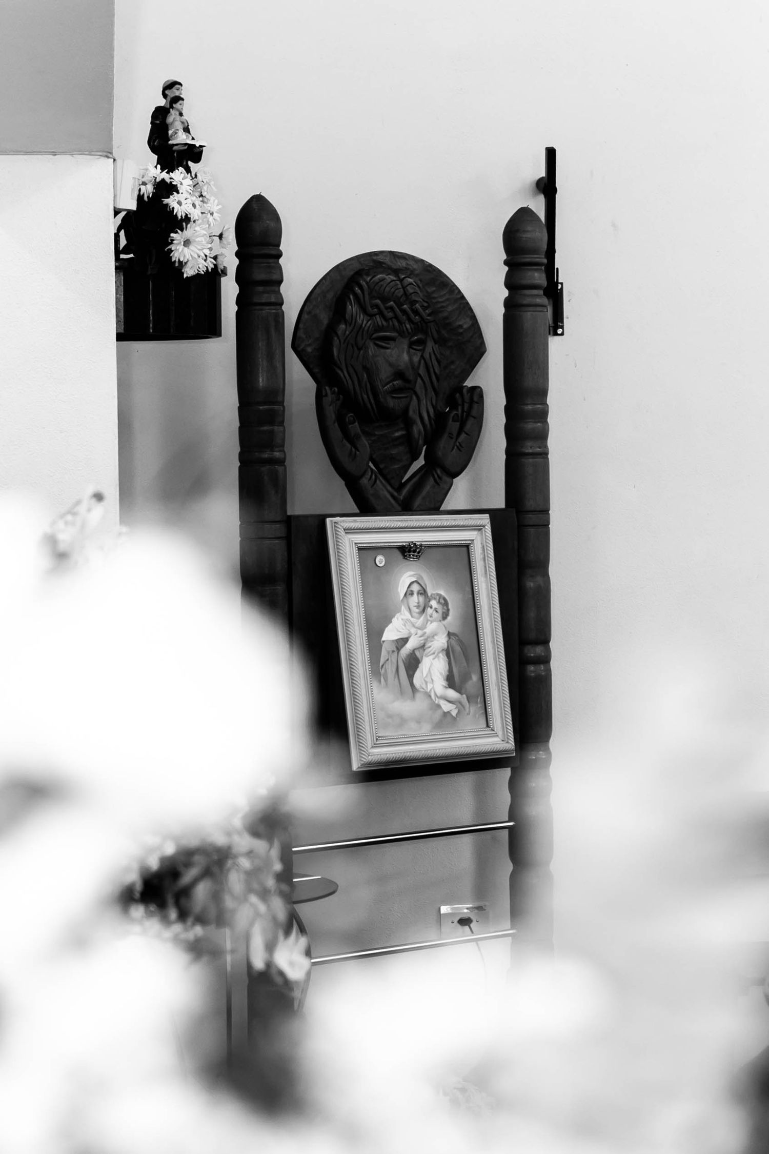 Black and white photo of religious icons including a Jesus relief sculpture and Virgin Mary framed picture on a wooden dresser.