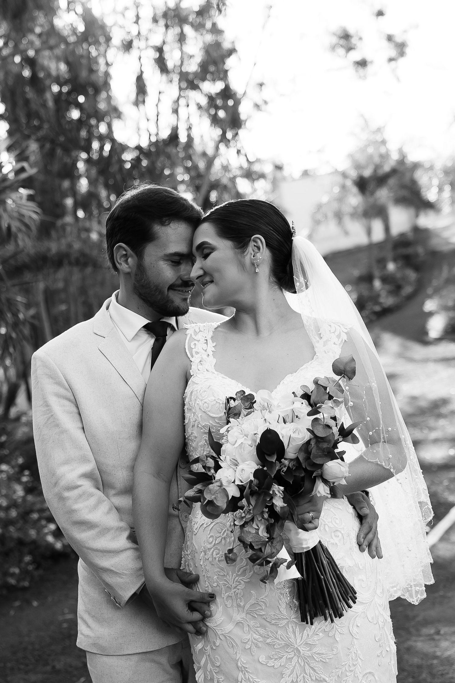 Black and white photo of a bride and groom sharing an intimate moment, bride holding a floral bouquet in a lace gown.
